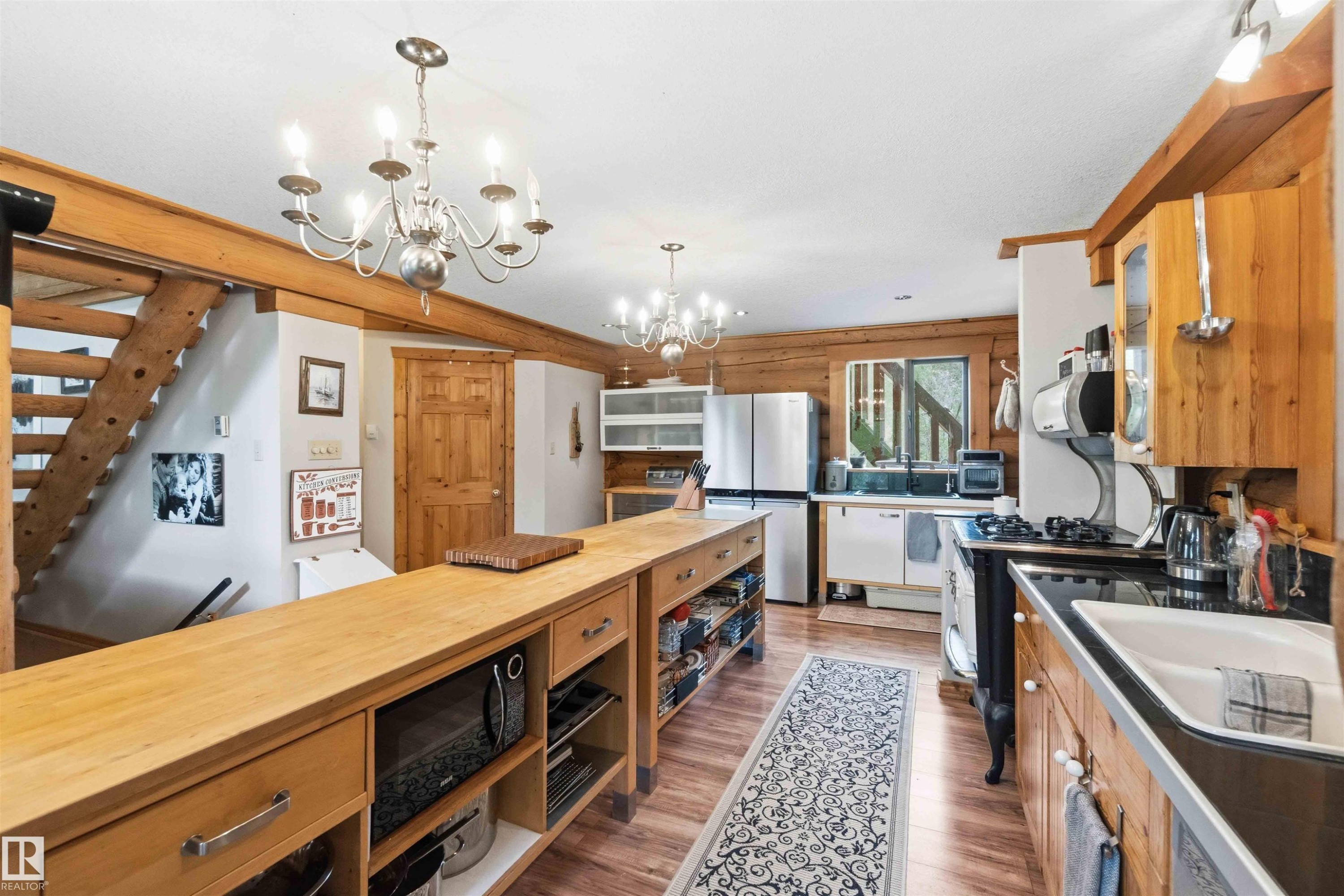 Open-concept kitchen featuring wood-finish flooring, exposed timber beams, wood cabinetry, and a large central island with butcher block countertop - #17 A 15031 Twp Road 462, Rural Wetaskiwin County, AB - Indoor Photo Showing Kitchen