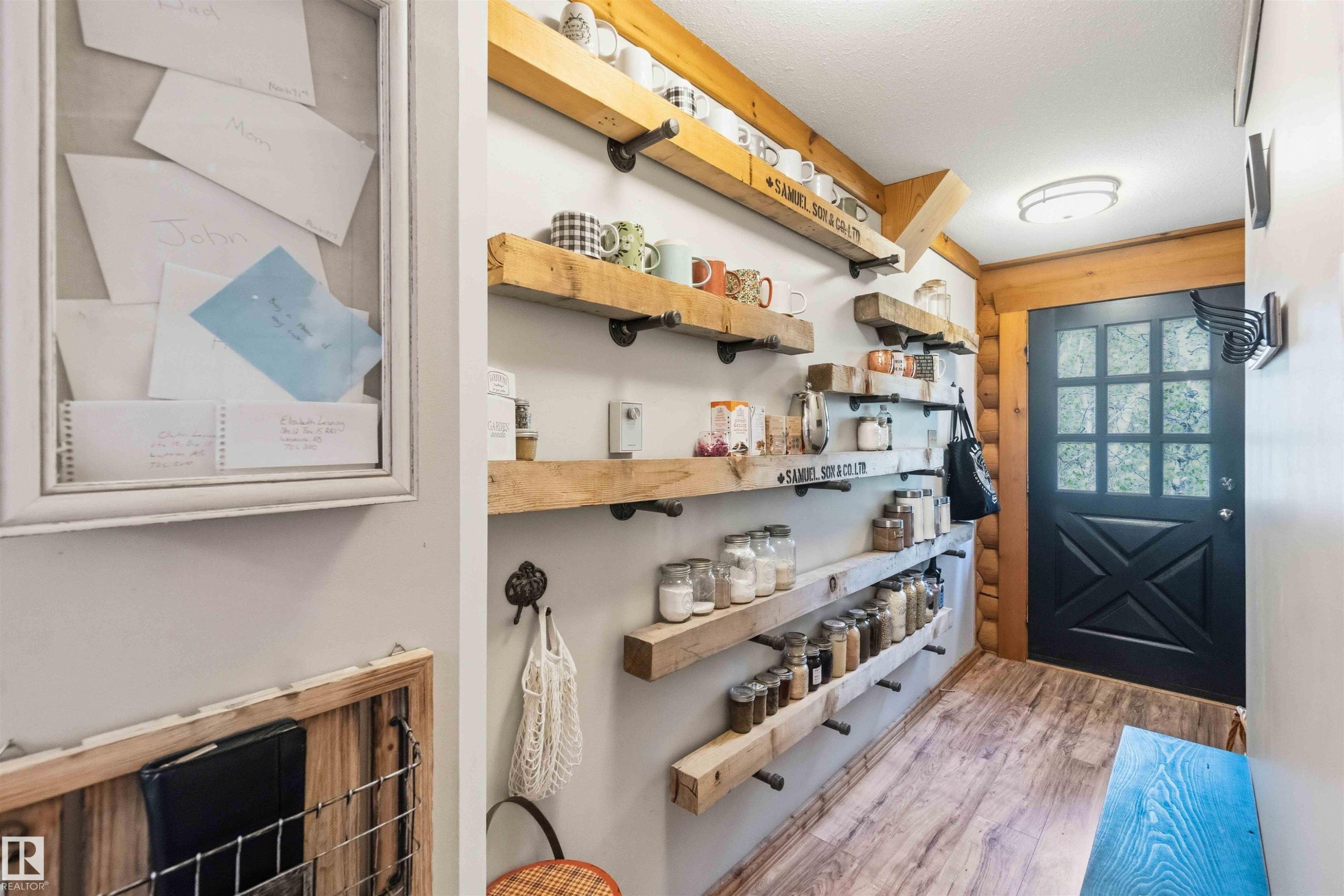 Entryway featuring wood-finish flooring, a black paneled door with glass inserts, exposed log wall detail, and an array of open shelving with industrial-style brackets - #17 A 15031 Twp Road 462, Rural Wetaskiwin County, AB - Indoor Photo Showing Other Room