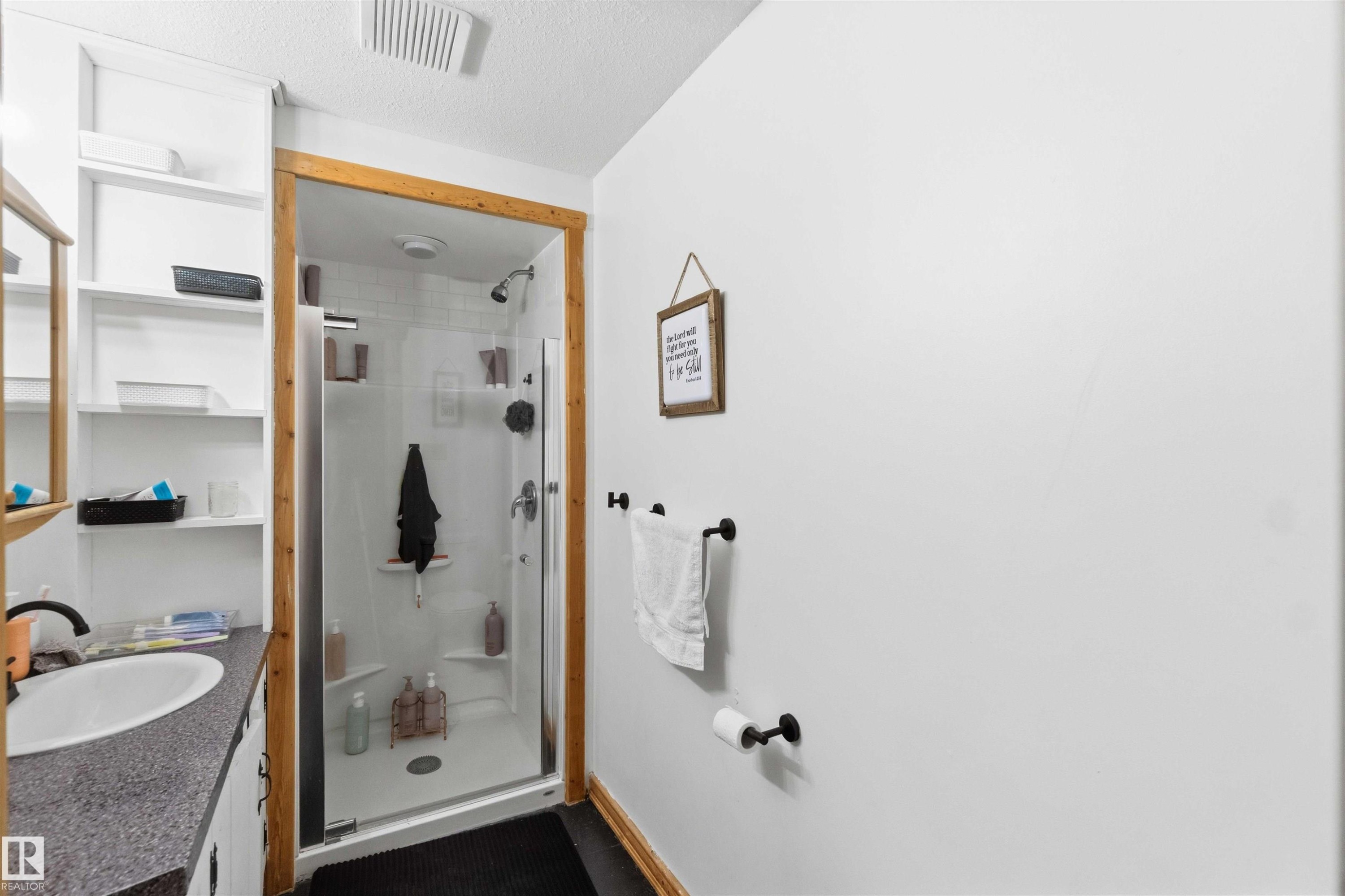 Bathroom featuring a glass-enclosed shower with white surround, a single vanity with a white basin and dark speckled countertop, and open shelving - #17 A 15031 Twp Road 462, Rural Wetaskiwin County, AB - Indoor Photo Showing Dining Room