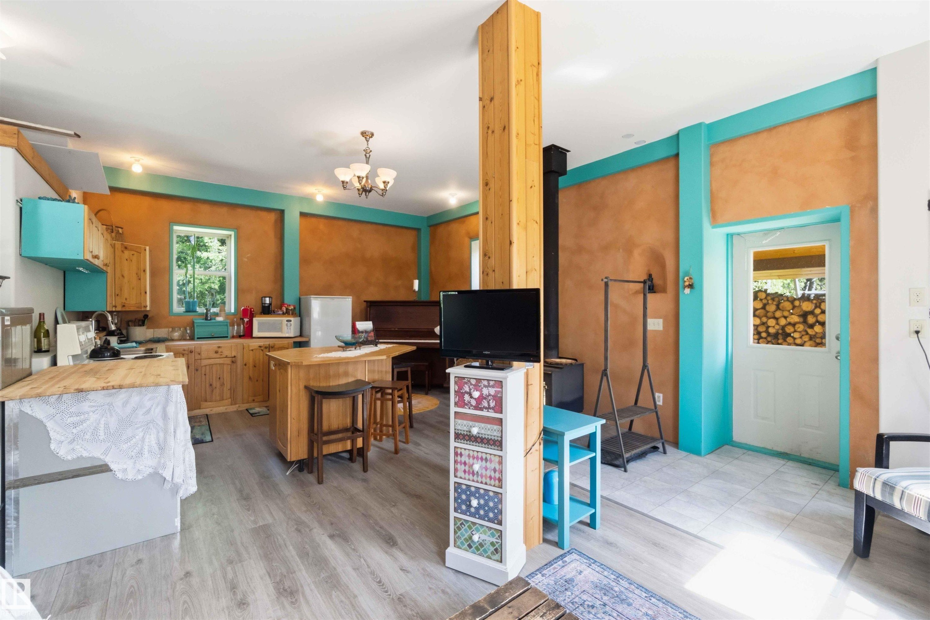 Open-concept living space featuring wood-finish flooring, a kitchen with natural wood cabinetry and a central island, and a wood-burning stove with a black stovepipe - #17 A 15031 Twp Road 462, Rural Wetaskiwin County, AB - Indoor