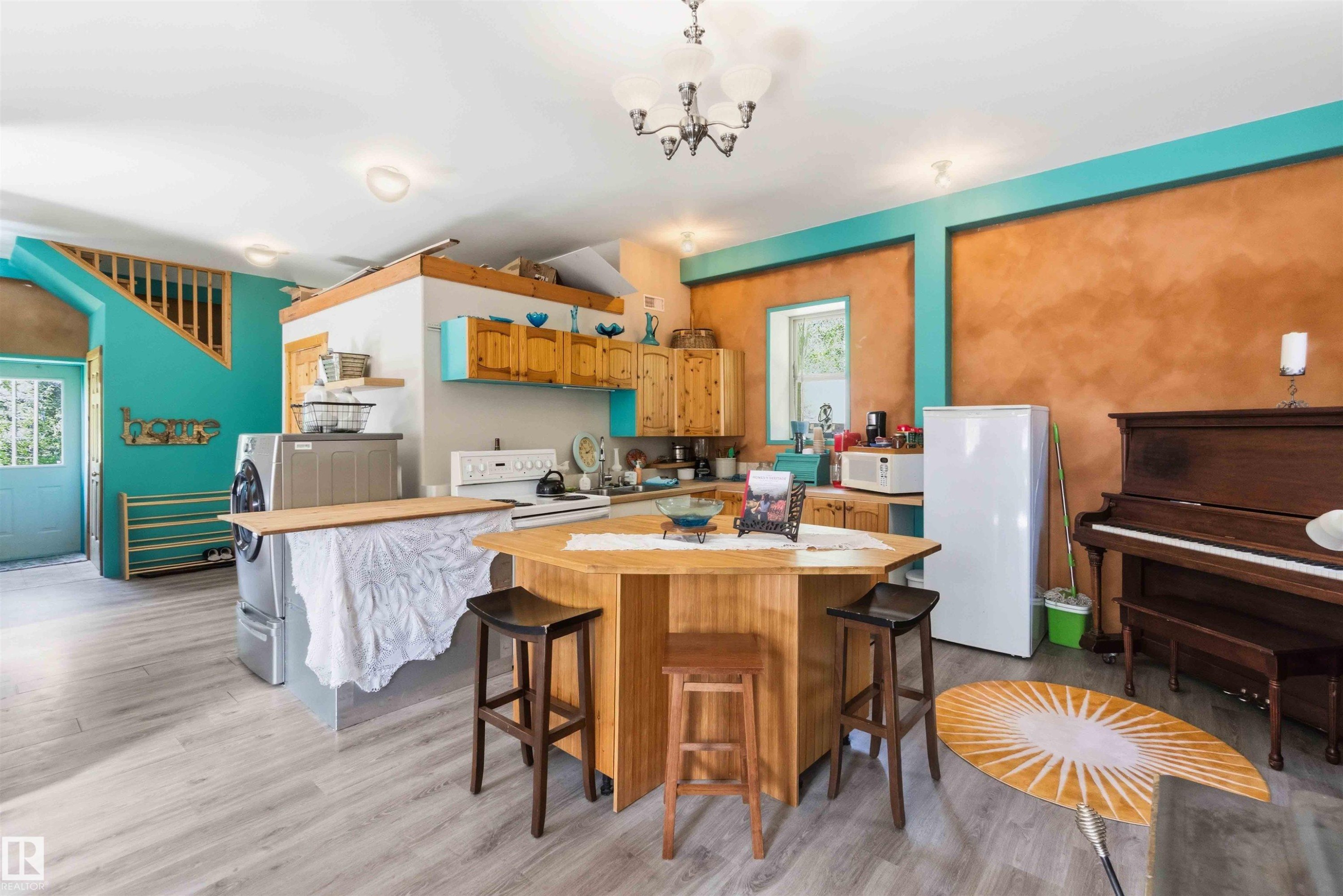 Open-concept living space featuring wood-finish flooring, a central kitchen island with seating, a built-in staircase, and light wood cabinetry - #17 A 15031 Twp Road 462, Rural Wetaskiwin County, AB - Indoor