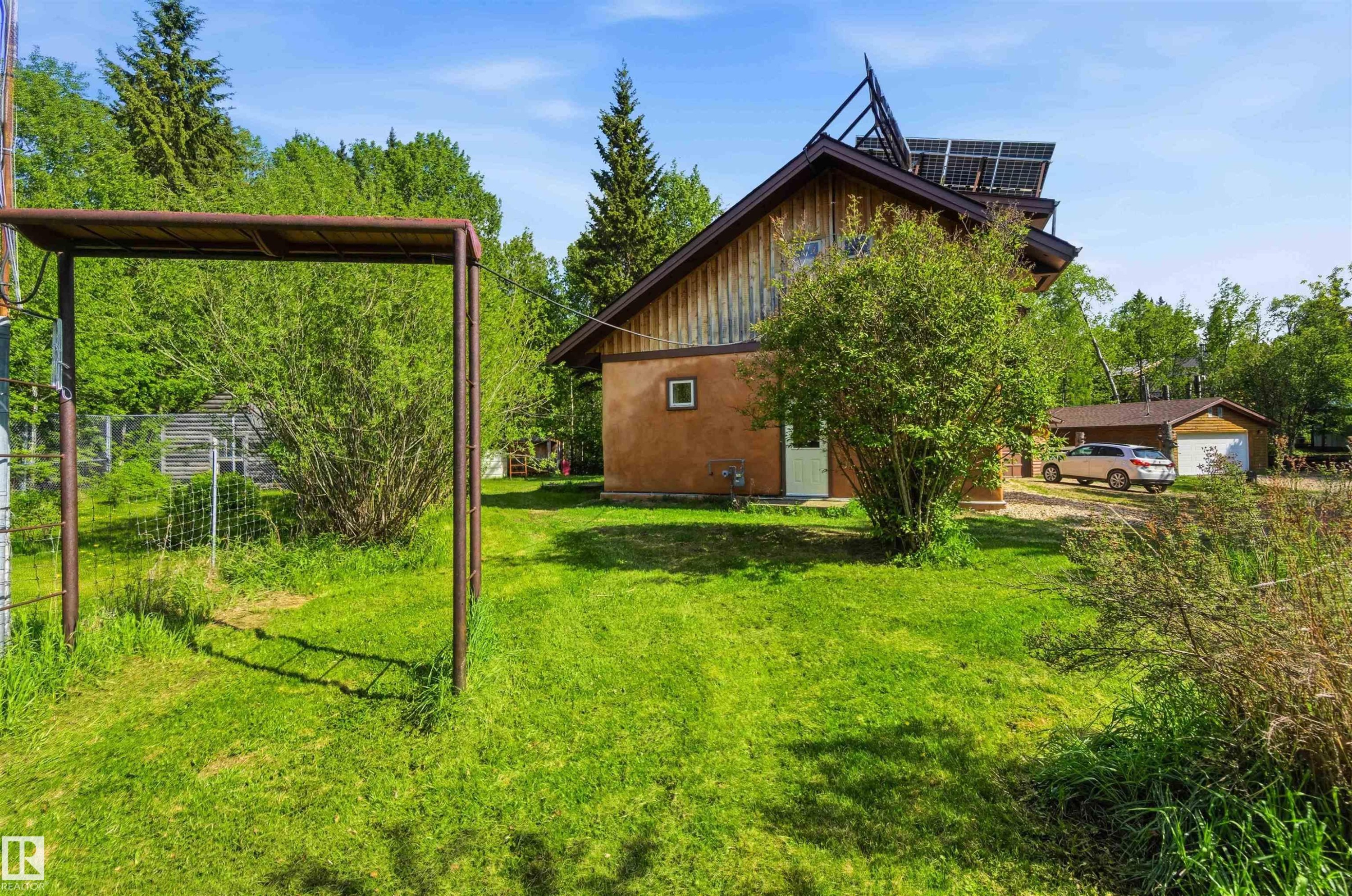 Exterior showcasing a stucco and wood-sided structure with rooftop solar panels, a white entry door, and an attached garage with a white overhead door - #17 A 15031 Twp Road 462, Rural Wetaskiwin County, AB - Outdoor