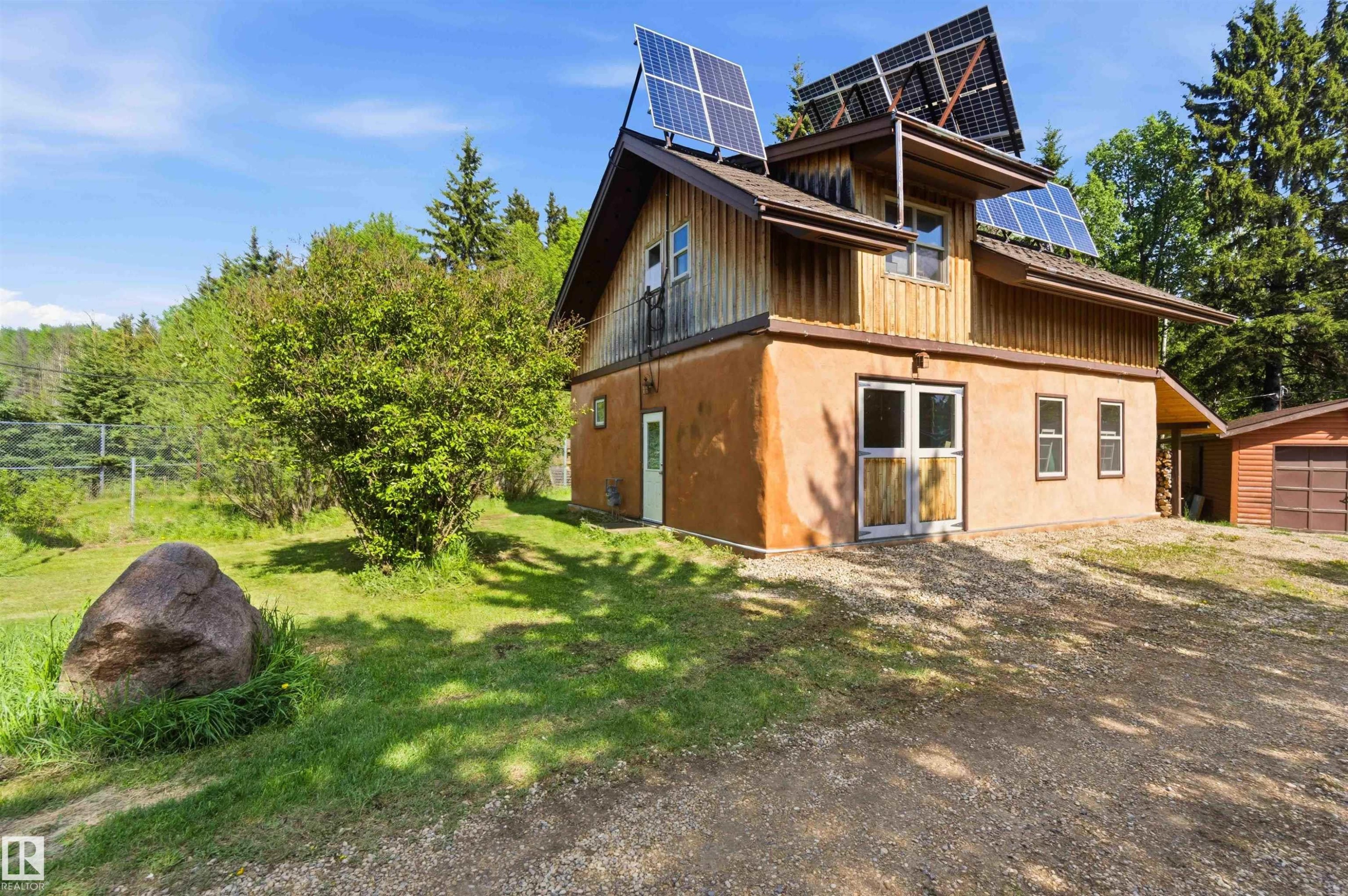 Two-story residence featuring an earth-toned lower level and a wood-sided upper level, with multiple roof-mounted solar panels - #17 A 15031 Twp Road 462, Rural Wetaskiwin County, AB - Outdoor