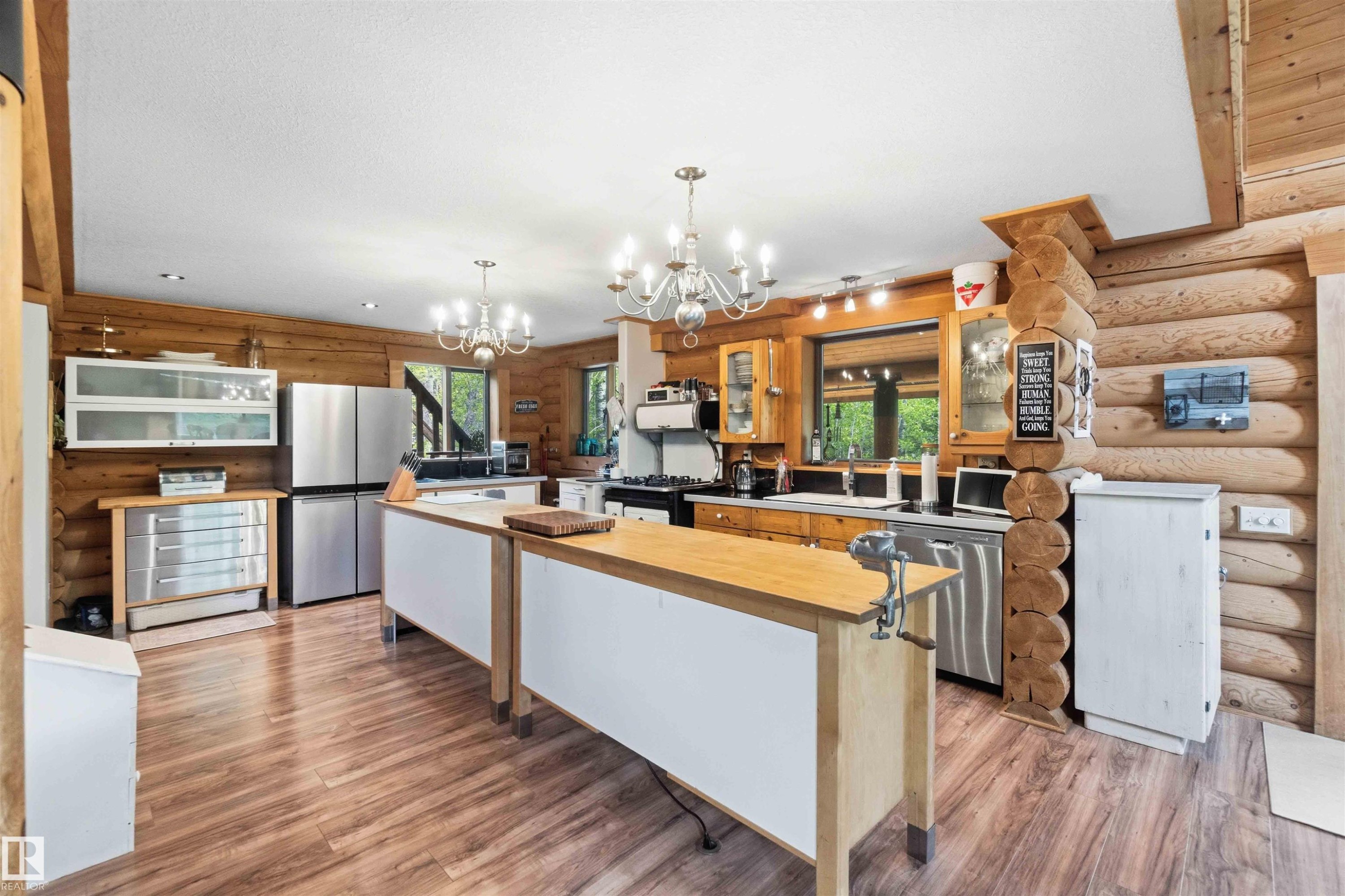 Spacious kitchen featuring two island work surfaces with butcher block tops, stainless steel appliances, wood-finish flooring, exposed log walls, and two multi-arm chandeliers - #17 A 15031 Twp Road 462, Rural Wetaskiwin County, AB - Indoor Photo Showing Living Room