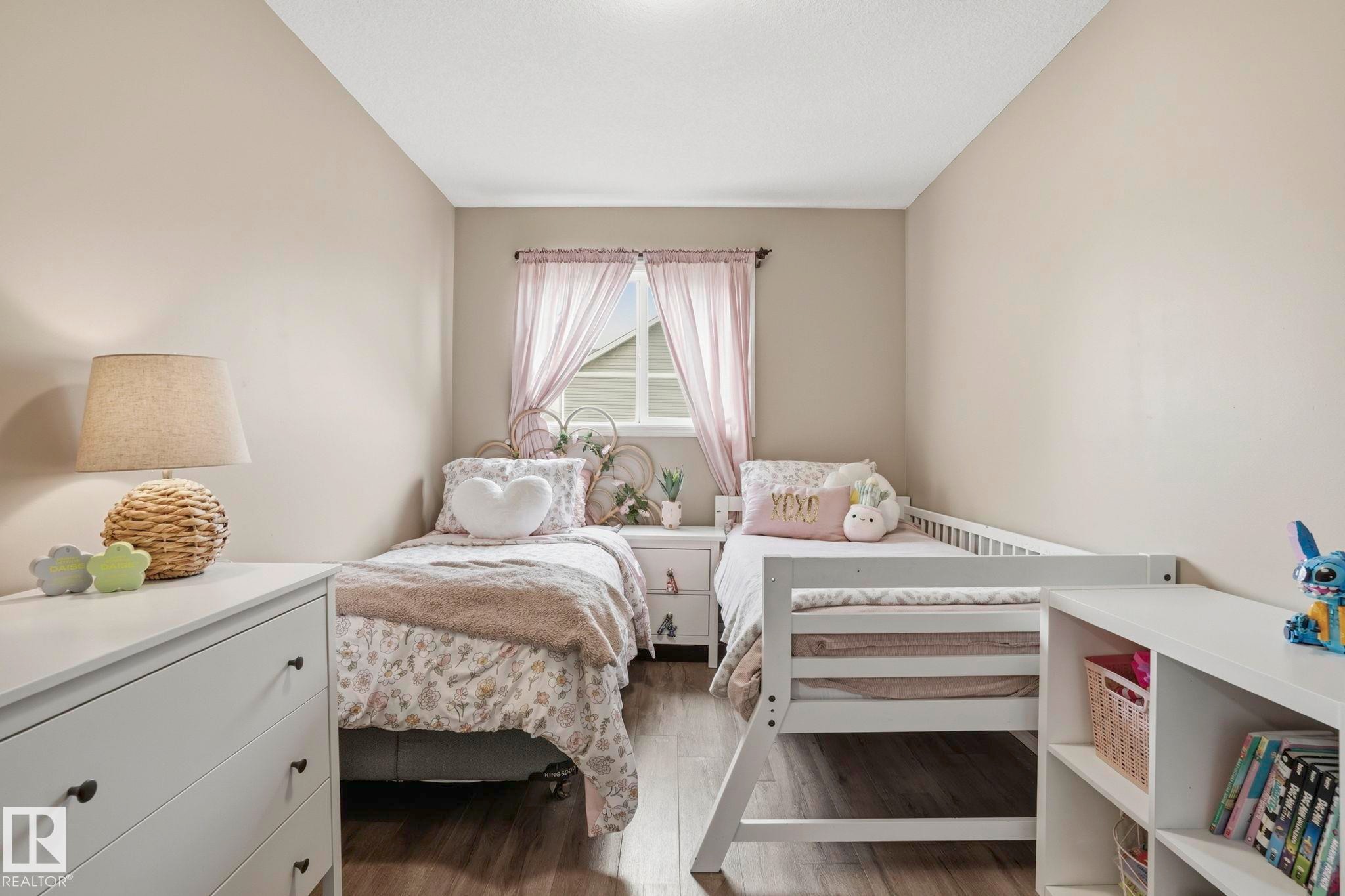 Bedroom featuring two twin beds, wood-finish flooring, a white window frame, and a built-in white shelving unit - 164 150 Edwards Drive, Edmonton, AB - Indoor Photo Showing Bedroom