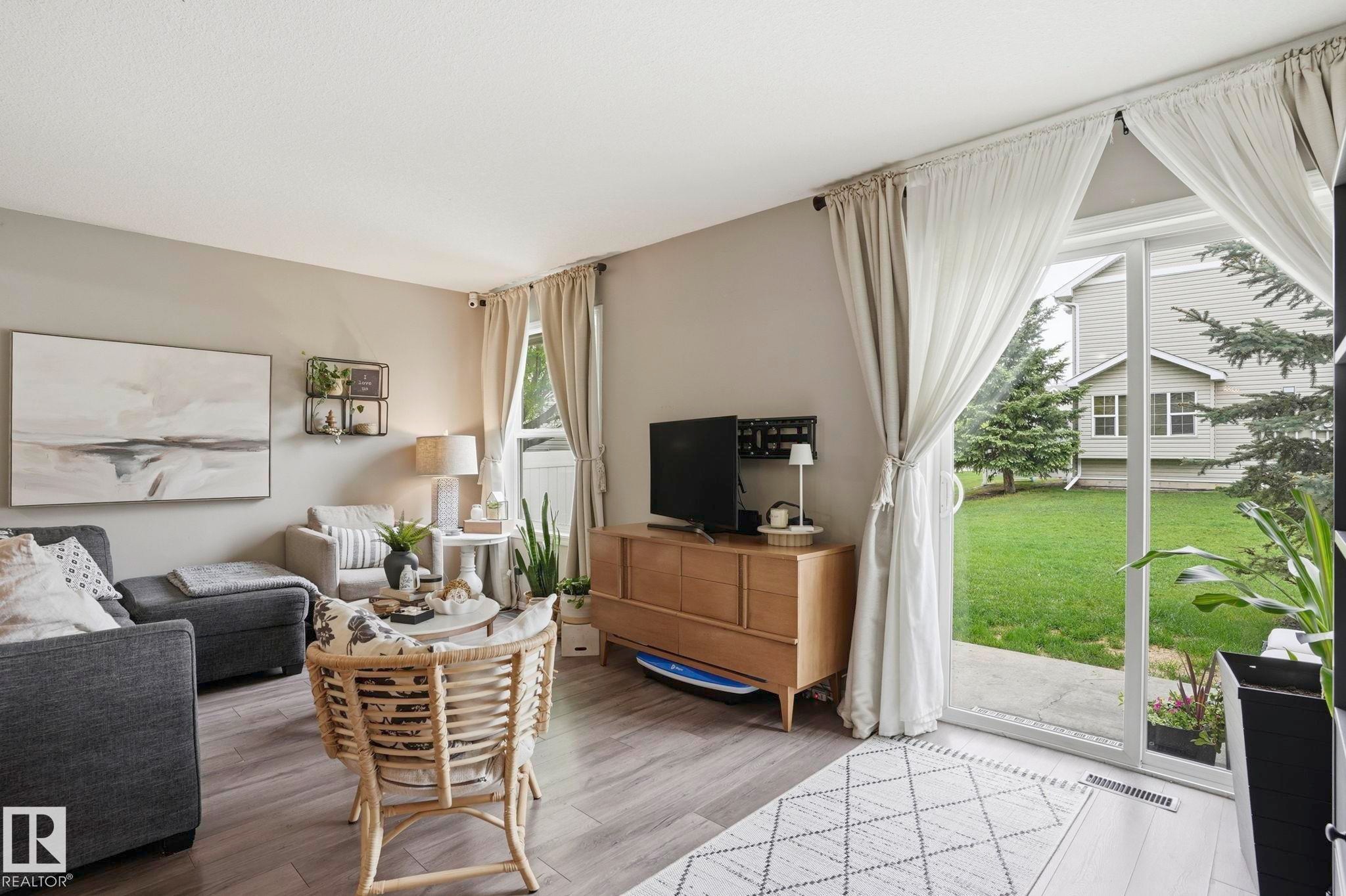 Spacious living area featuring wood-finish flooring, light neutral wall tones, and a sliding glass door providing outdoor access - 164 150 Edwards Drive, Edmonton, AB - Indoor Photo Showing Living Room