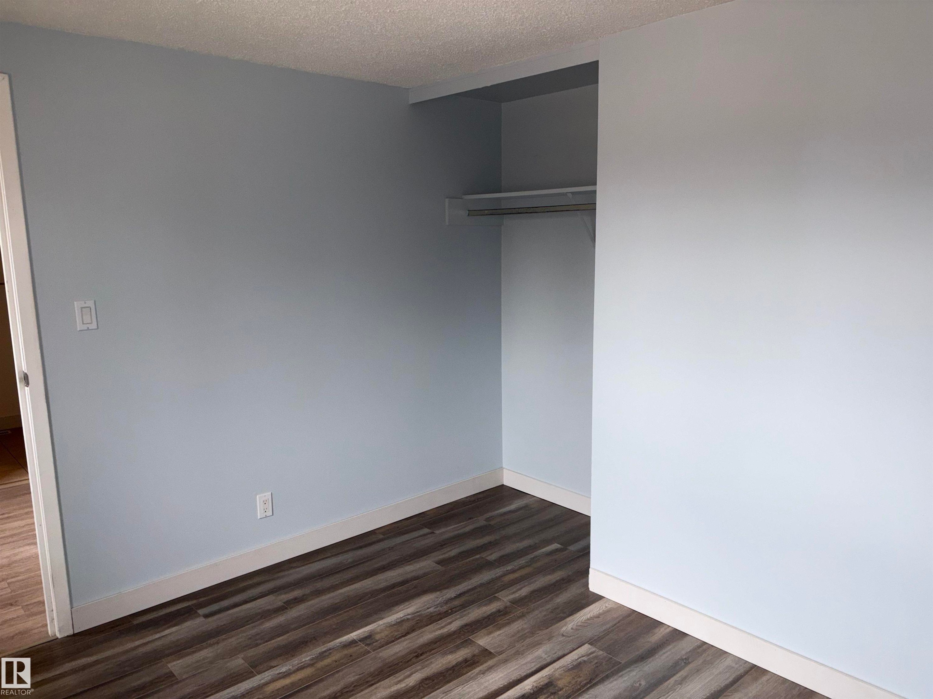 Interior space featuring wood-finish flooring, light blue wall paint, white baseboards, and an open closet with a hanging rod - 167 Ridgewood, St. Albert, AB - Indoor Photo Showing Other Room