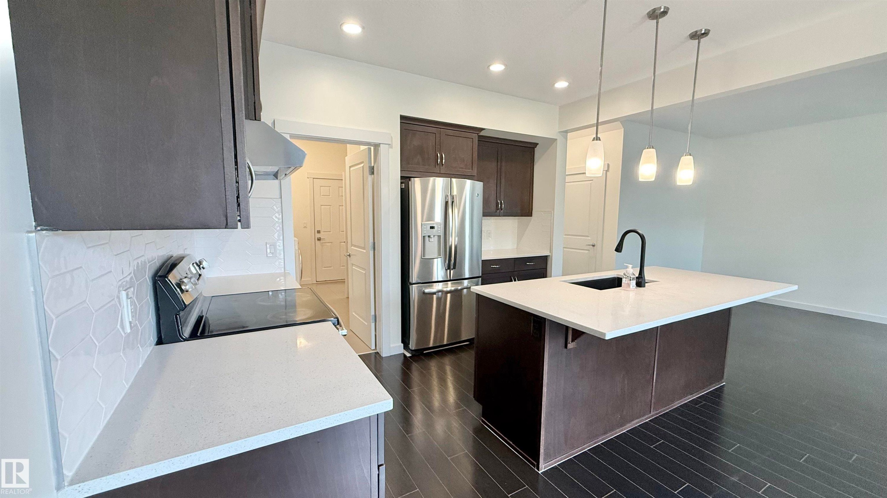 Modern kitchen featuring dark wood-finish cabinetry, stainless steel appliances, and light-toned countertops - 3962 Claxton Loop, Edmonton, AB - Indoor Photo Showing Kitchen With Stainless Steel Kitchen