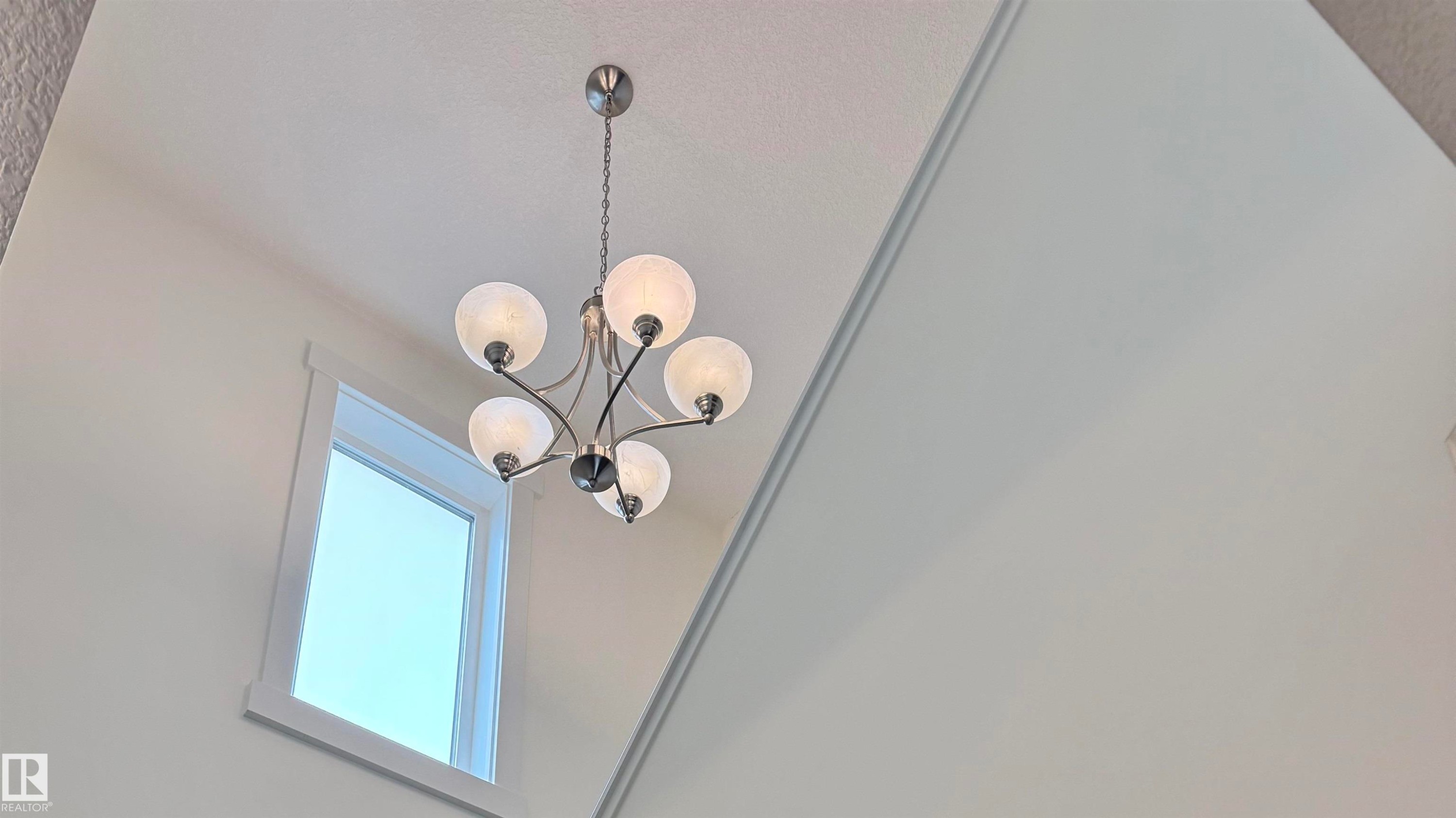 Vaulted ceiling with a contemporary chandelier featuring five spherical glass shades, natural light from a rectangular window, and crisp white wall paint - 3962 Claxton Loop, Edmonton, AB - Indoor Photo Showing Other Room