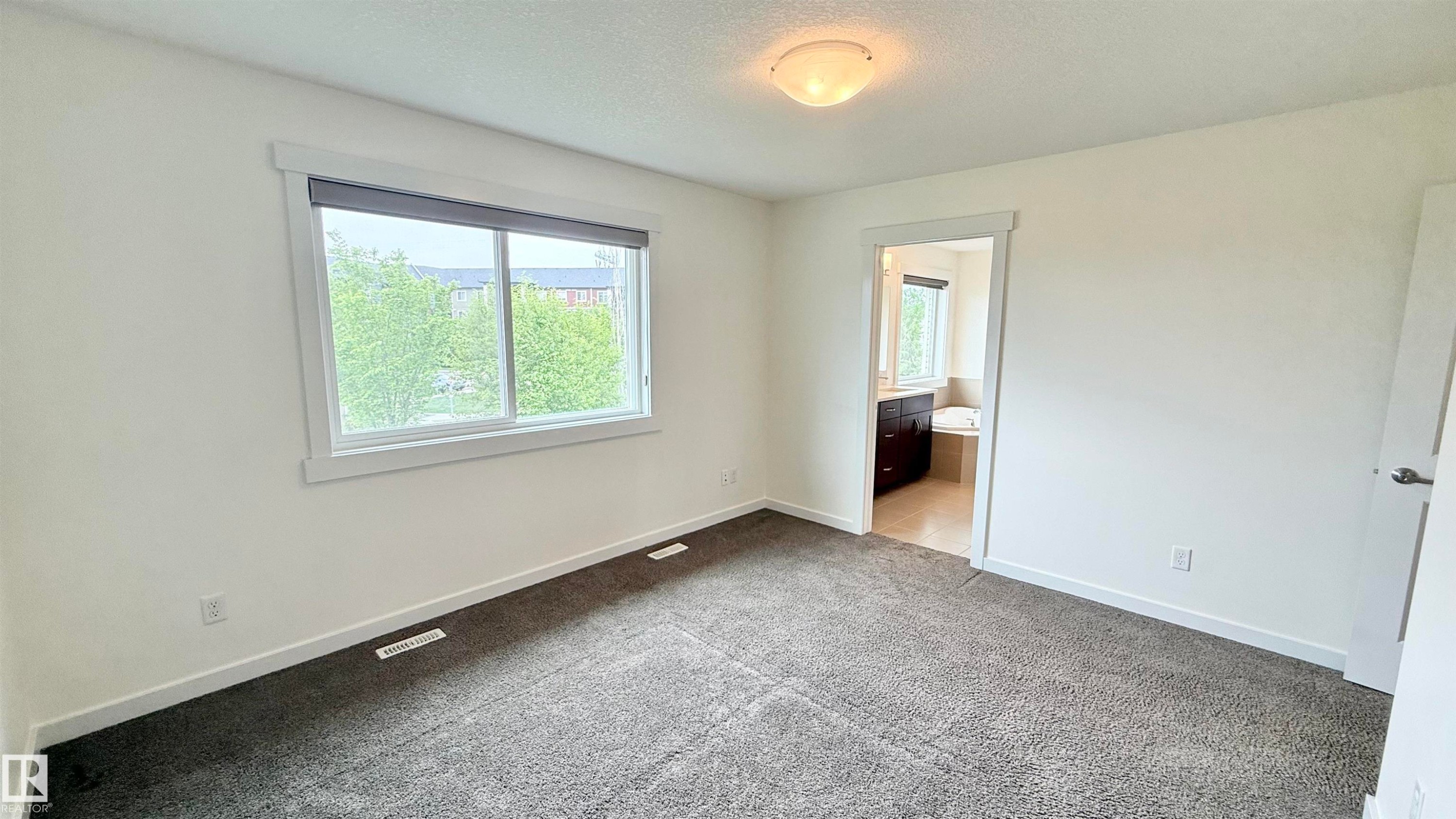 Spacious room featuring neutral carpeting, white walls, and a large window with roller shades - 3962 Claxton Loop, Edmonton, AB - Indoor Photo Showing Other Room
