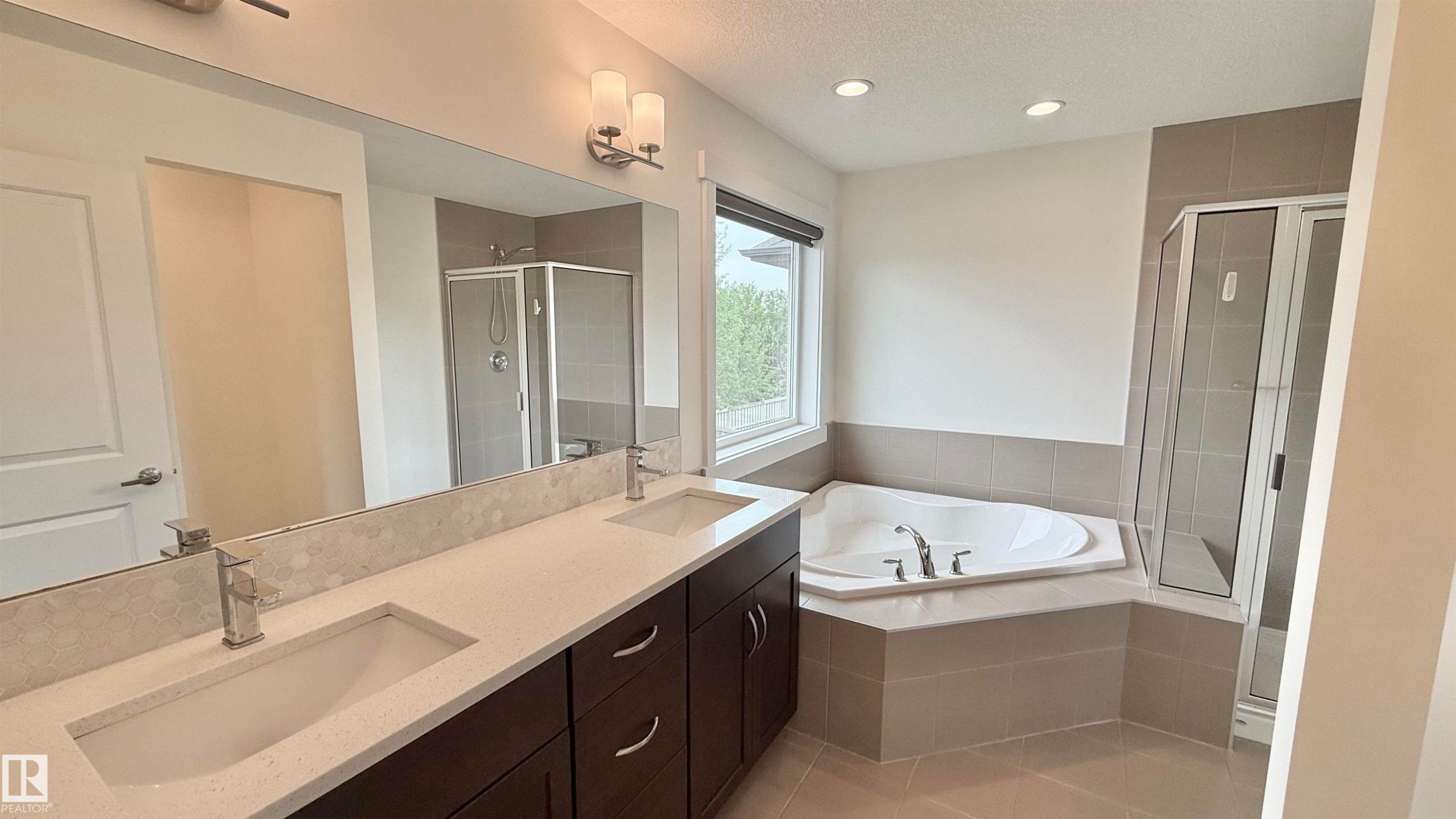 Bathroom featuring a dual vanity with undermount sinks, a built-in corner soaking tub, a separate glass-enclosed shower, a large mirror, and recessed lighting - 3962 Claxton Loop, Edmonton, AB - Indoor Photo Showing Bathroom