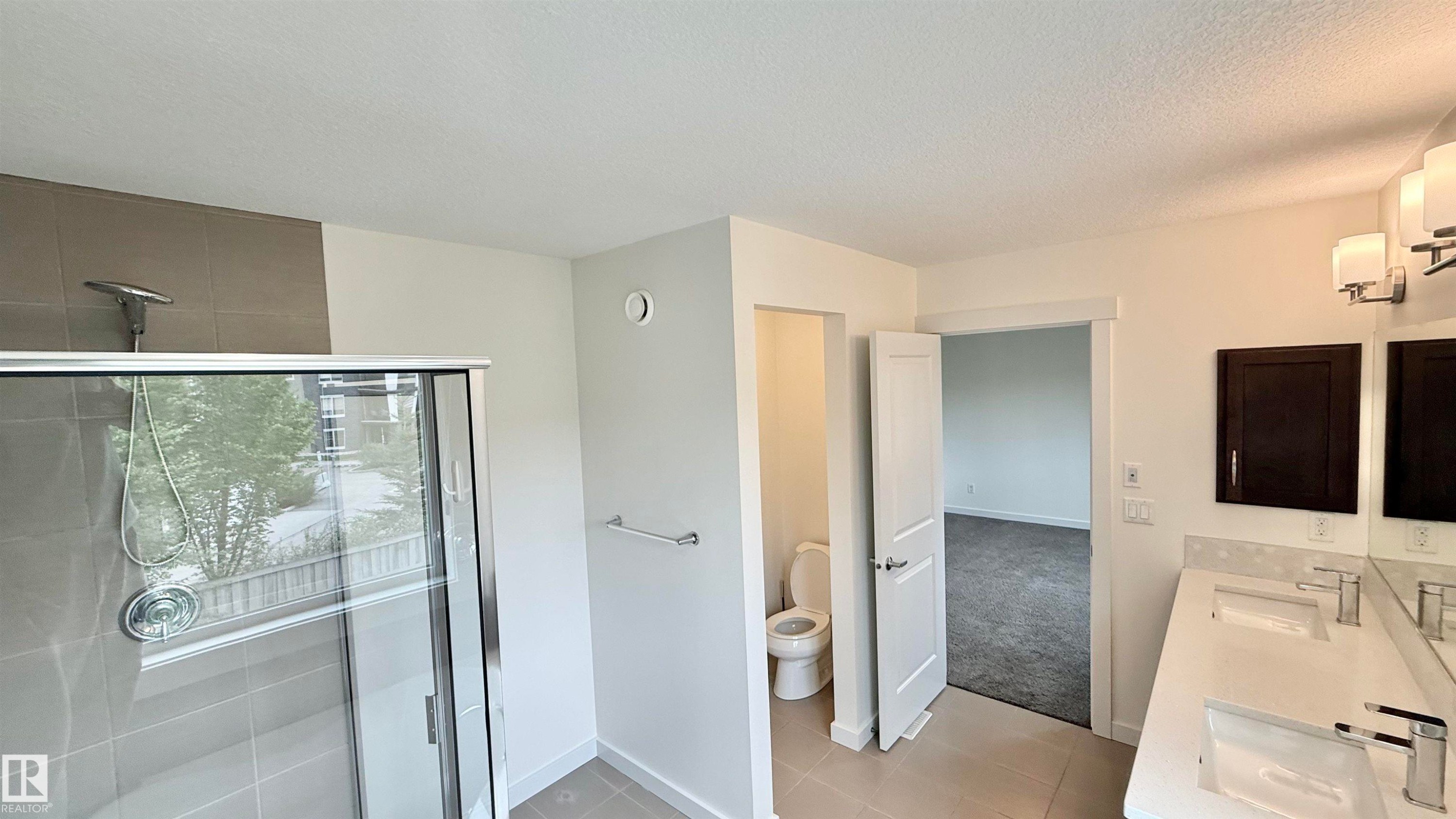 Contemporary bathroom featuring a spacious glass-enclosed shower with tile surround, a dual vanity with undermount sinks and modern fixtures, and neutral floor tiling - 3962 Claxton Loop, Edmonton, AB - Indoor
