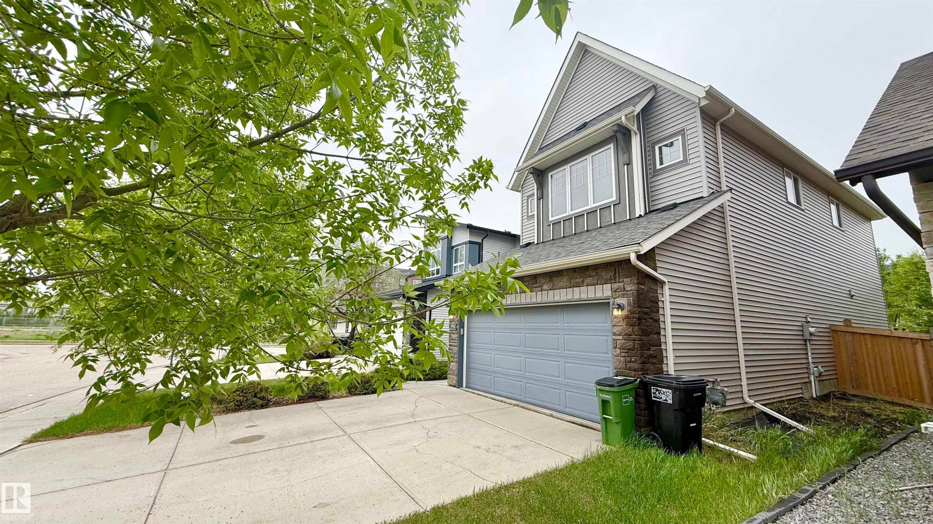 Contemporary two-story exterior featuring a single-car garage with an overhead door, stone veneer accents, and horizontal siding - 3962 Claxton Loop, Edmonton, AB - Outdoor