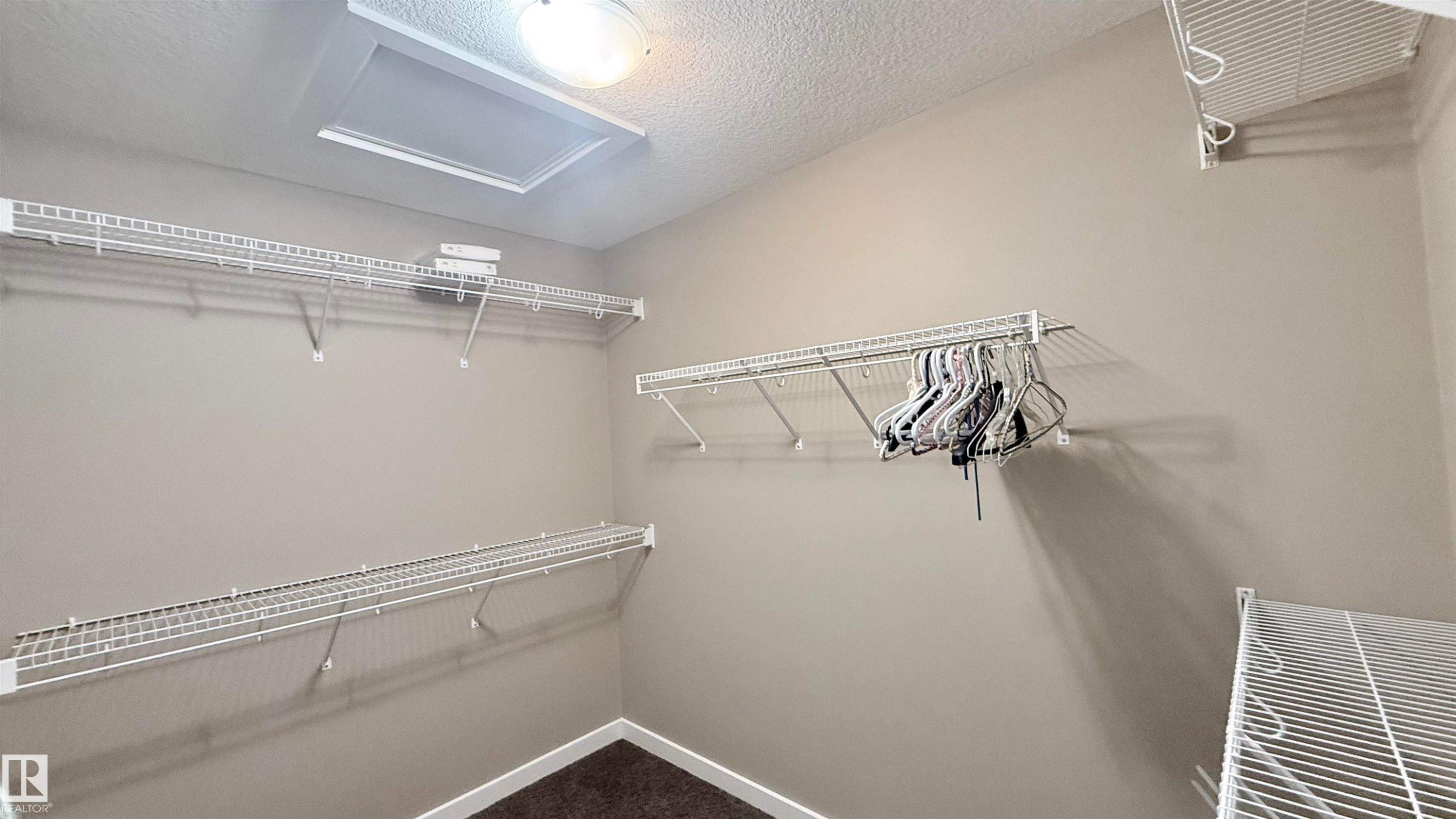 Walk-in closet featuring wire shelving, wire hanging rods, neutral wall paint, overhead lighting, and dark carpet flooring - 3962 Claxton Loop, Edmonton, AB - Indoor With Storage