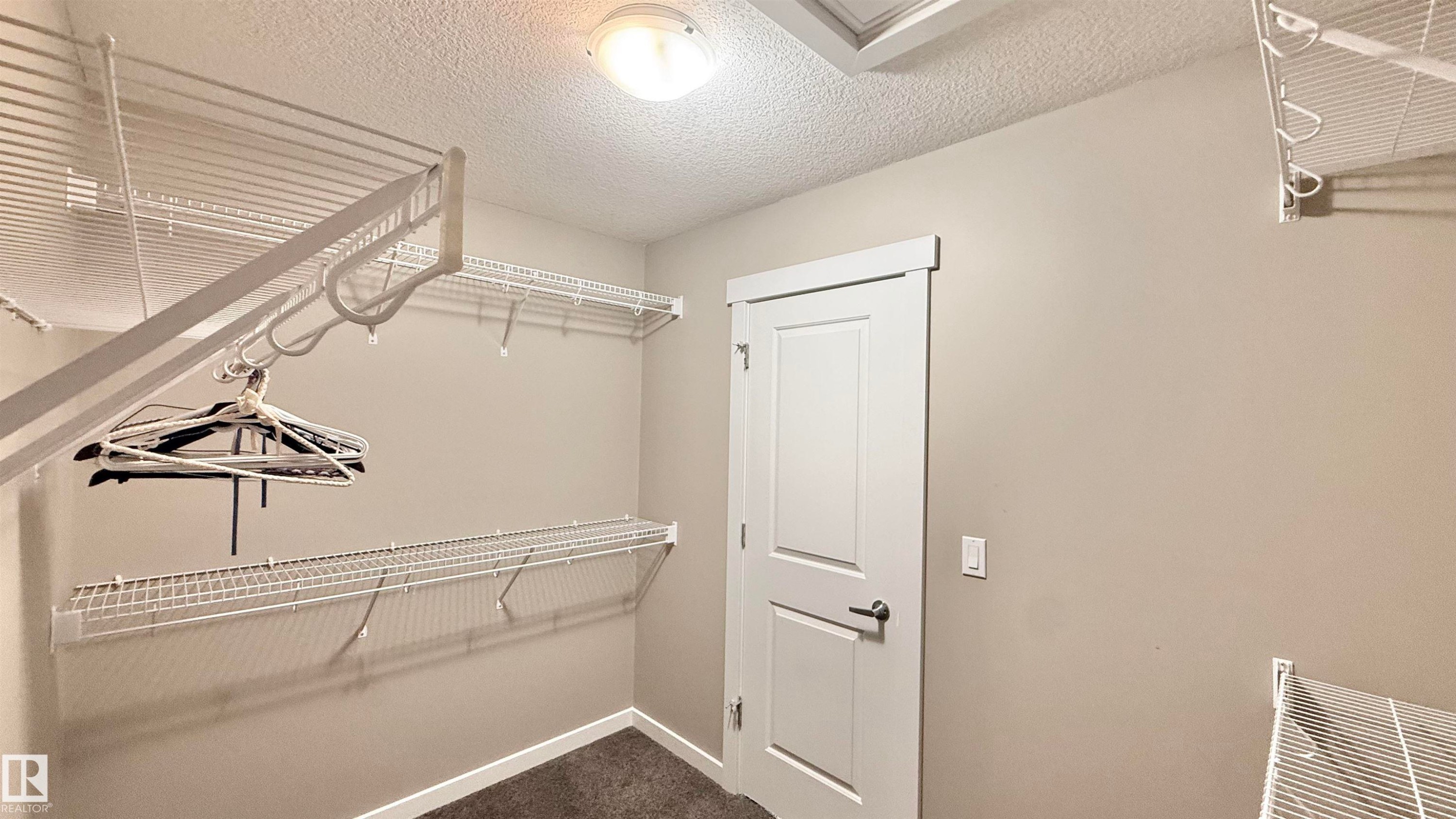Spacious closet featuring white wire shelving, hanging rods, light gray walls, and dark carpet flooring - 3962 Claxton Loop, Edmonton, AB - Indoor