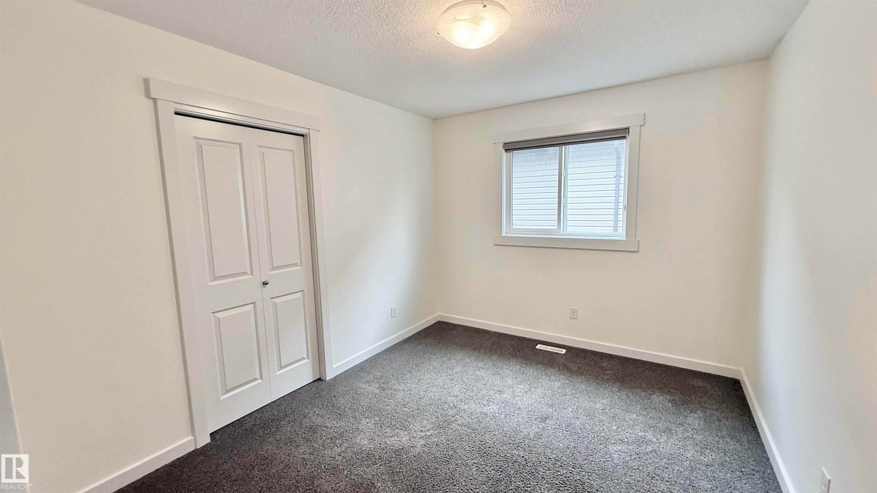 Bright room featuring neutral wall tones, dark textured carpeting, a double bifold closet, and a window with blinds - 3962 Claxton Loop, Edmonton, AB - Indoor Photo Showing Other Room