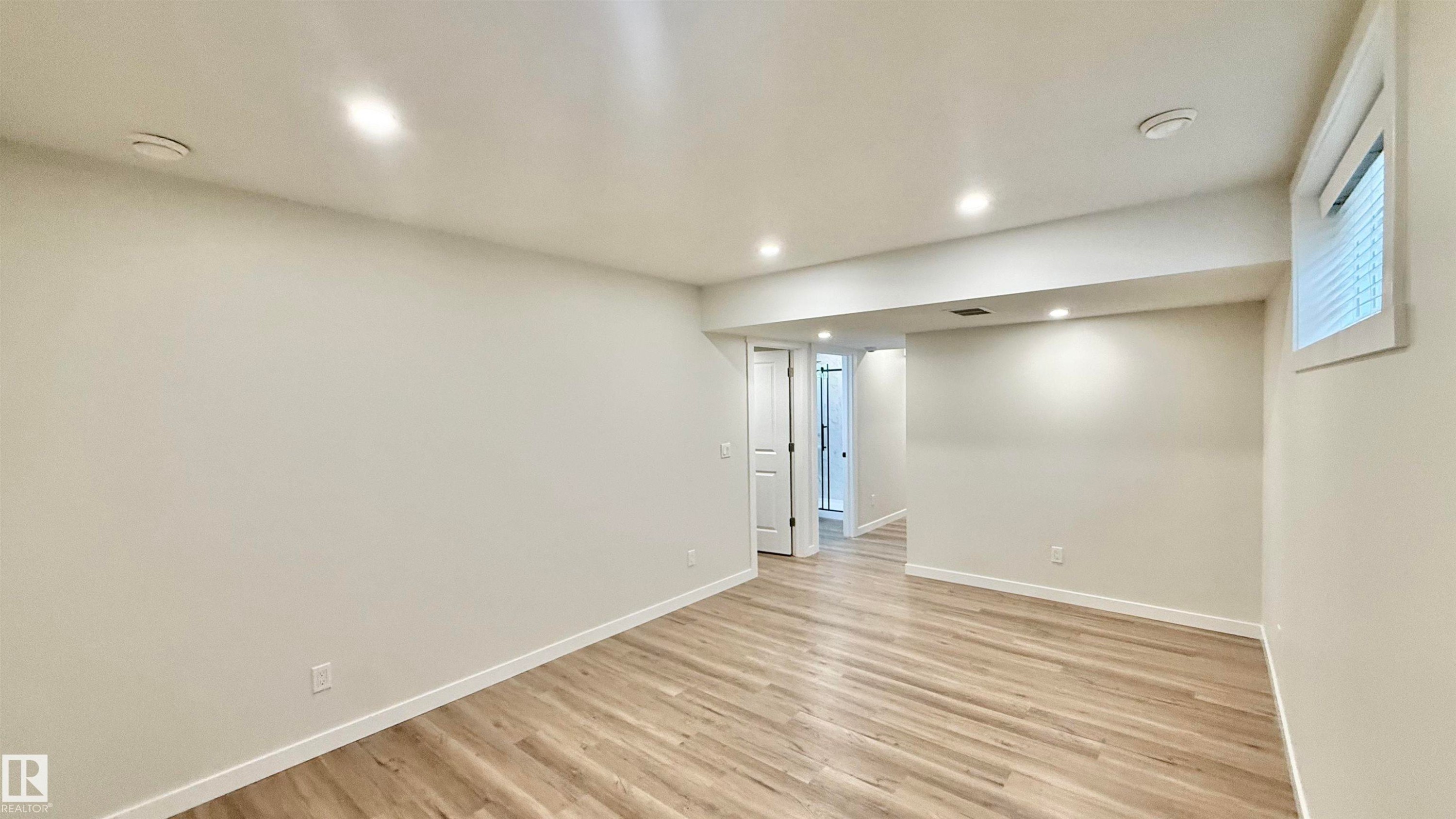 Spacious room featuring wood-finish flooring, recessed ceiling lighting, a window with horizontal blinds, and a white interior door - 3962 Claxton Loop, Edmonton, AB - Indoor Photo Showing Other Room