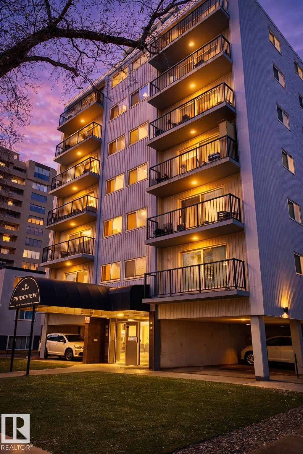 Multi-story residential building featuring private balconies with metal railings, a covered entrance with an awning, and recessed parking - 202 8310 Jasper Avenue, Edmonton, AB - Outdoor With Balcony