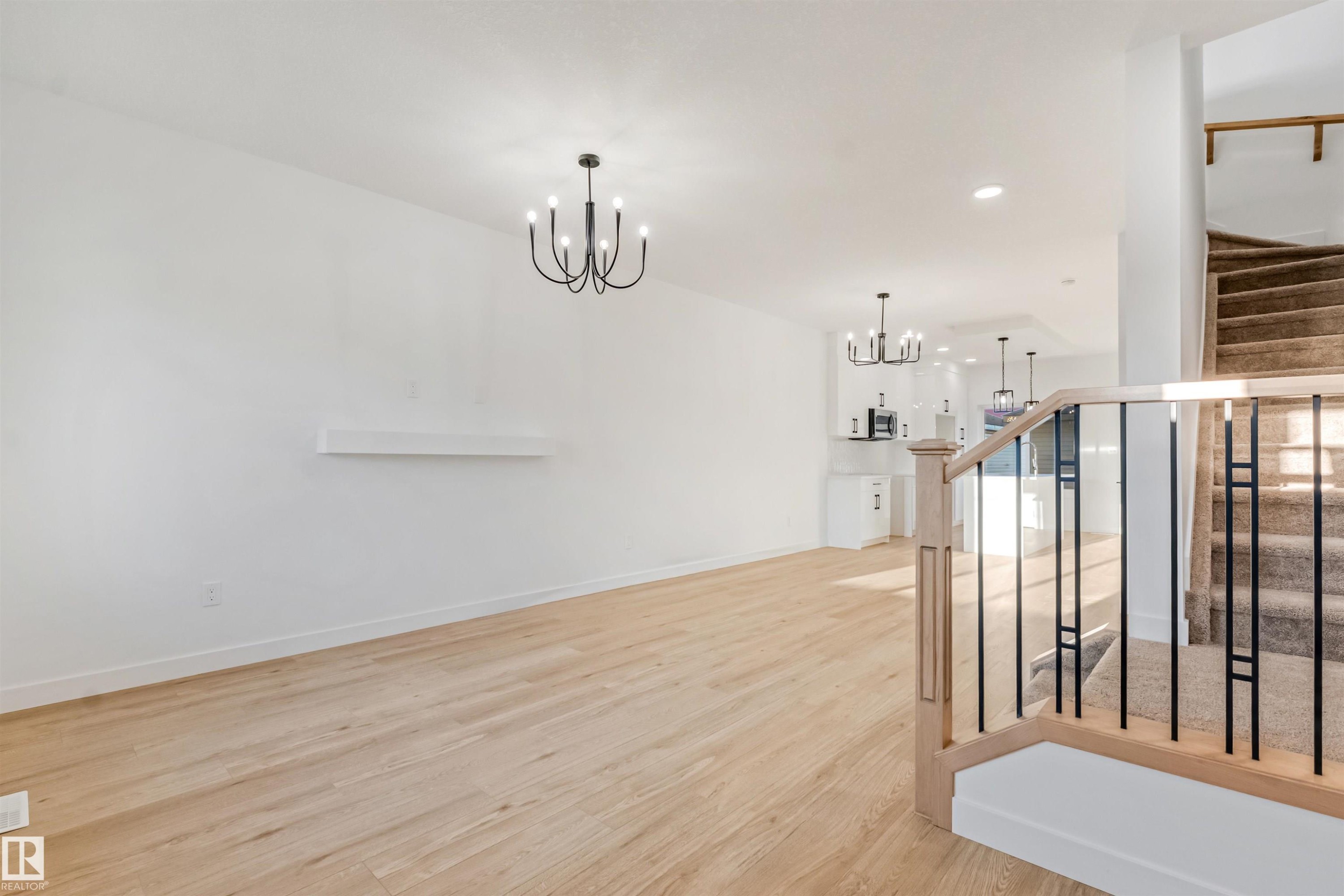 Spacious room with wood-finish flooring and a contemporary chandelier - 1511 211 Street Nw, Edmonton, AB