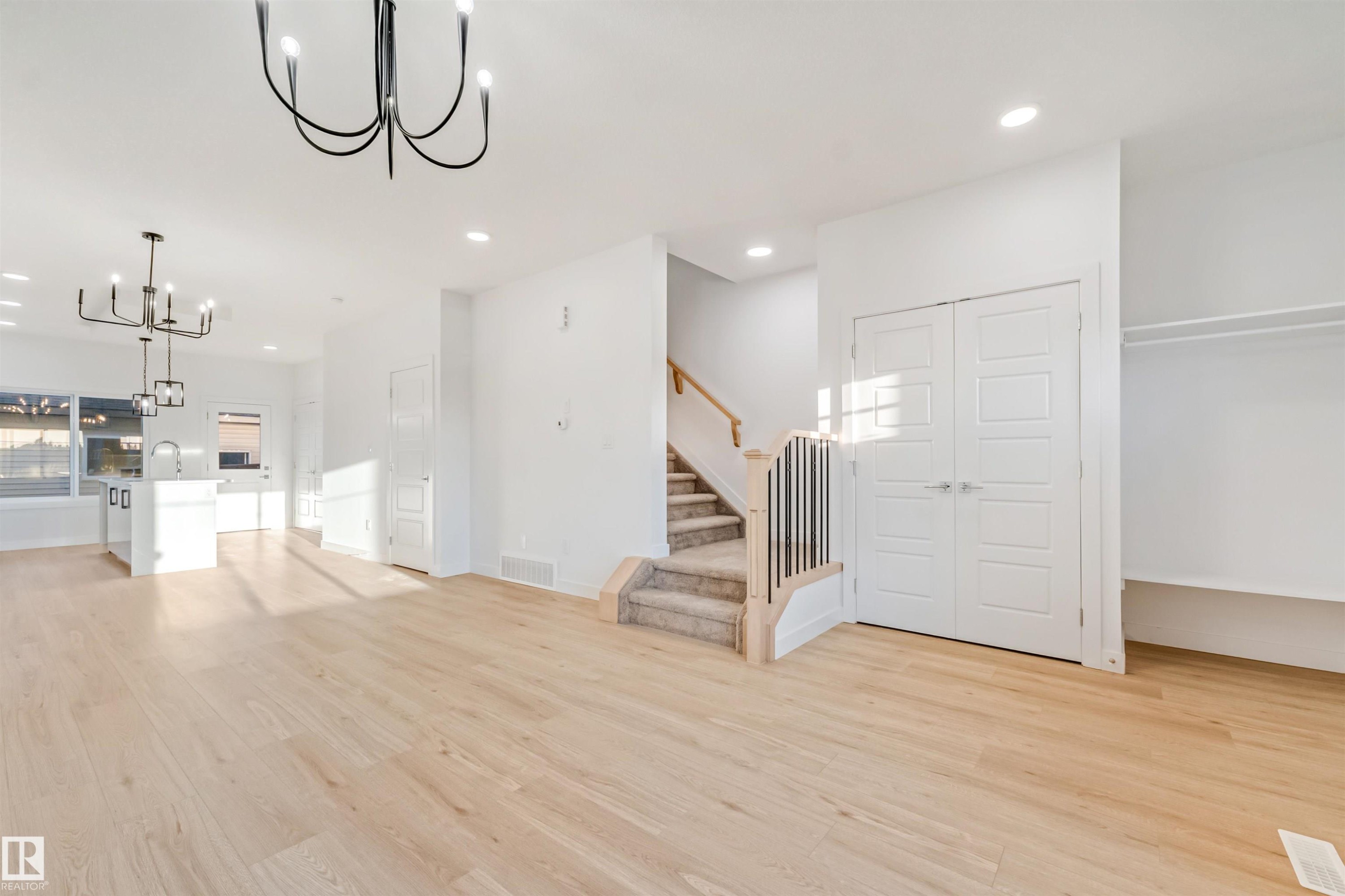 Open-concept living space with light wood-finish flooring, recessed lighting, and a modern chandelier - 1511 211 Street Nw, Edmonton, AB