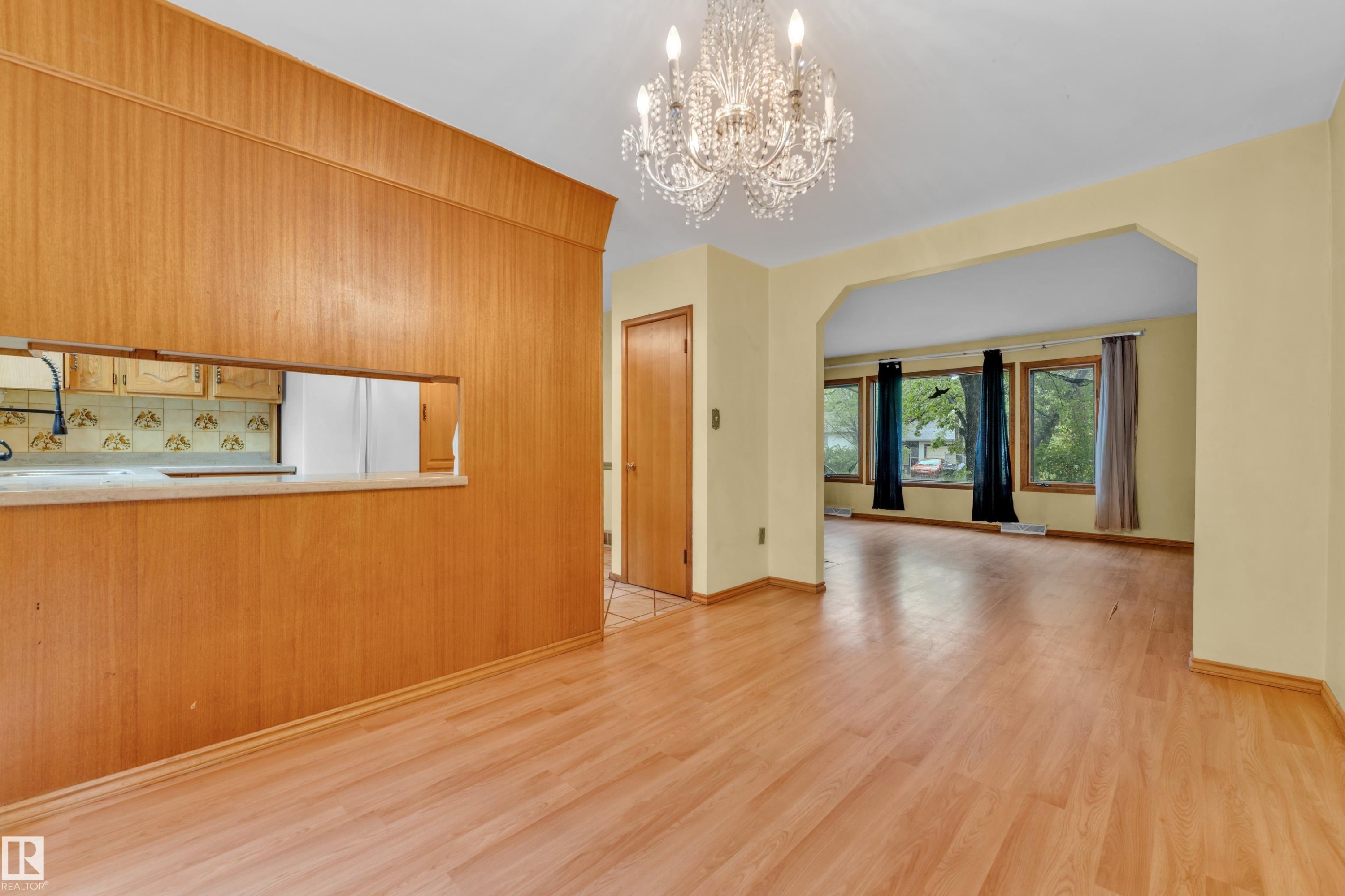 Spacious living area featuring wood-finish flooring, an arched entryway, and multiple windows - 10819 54 Avenue, Edmonton, AB