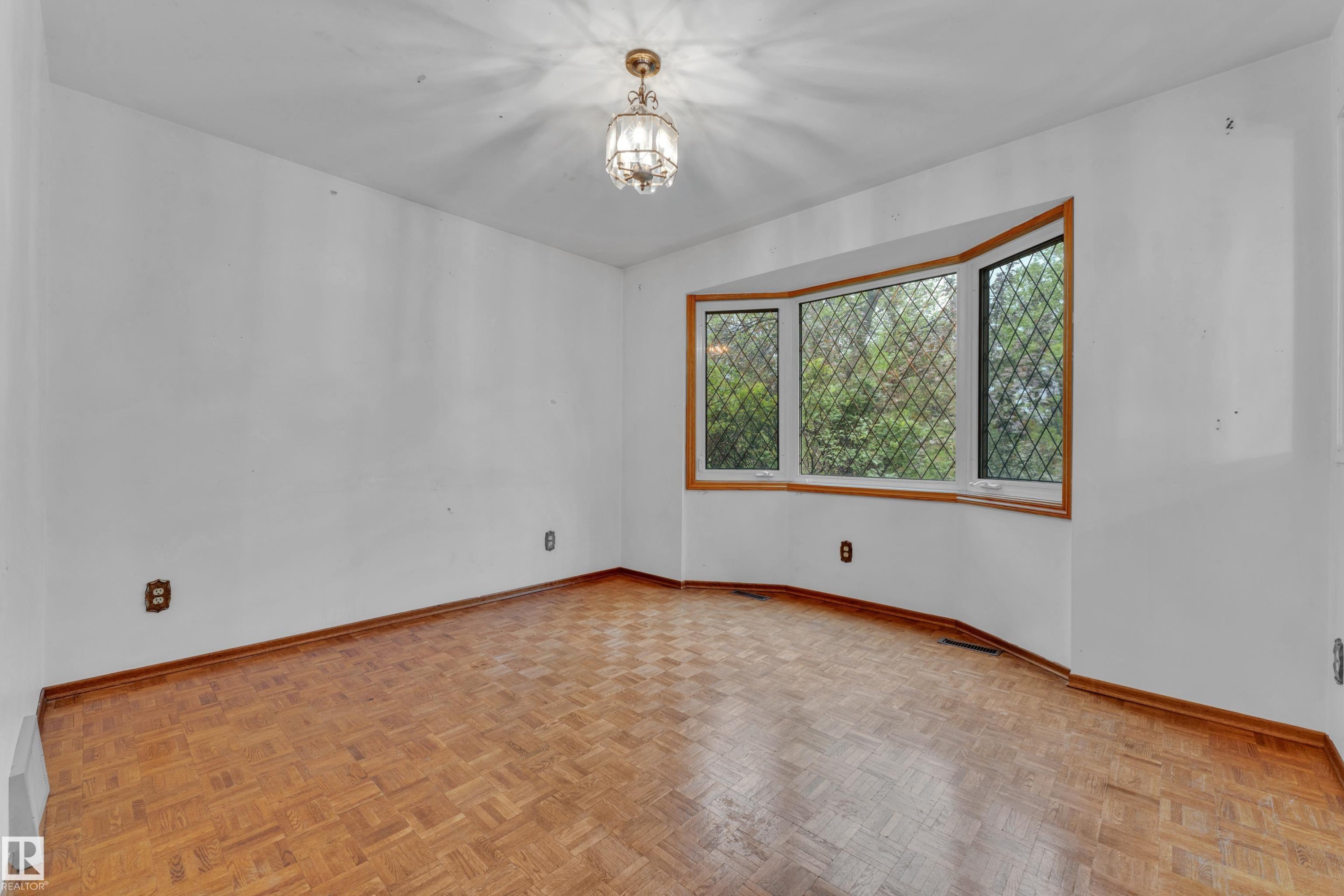 Room featuring a prominent bay window with diamond-patterned muntins, wood-finish flooring, and a central ceiling light fixture - 10819 54 Avenue, Edmonton, AB