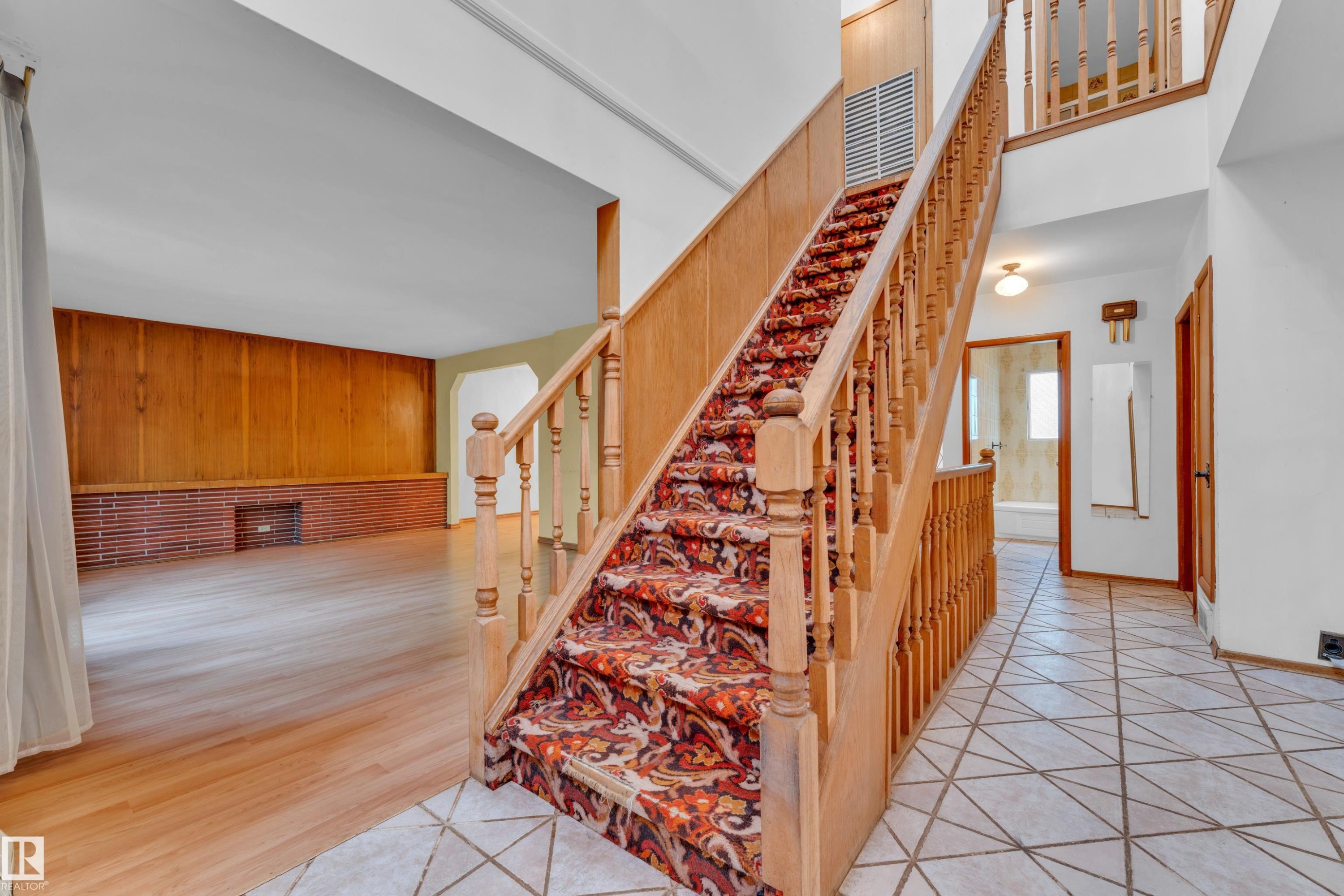Entry foyer featuring geometric floor tiling, a wooden staircase with patterned runner, and a double-height ceiling - 10819 54 Avenue, Edmonton, AB