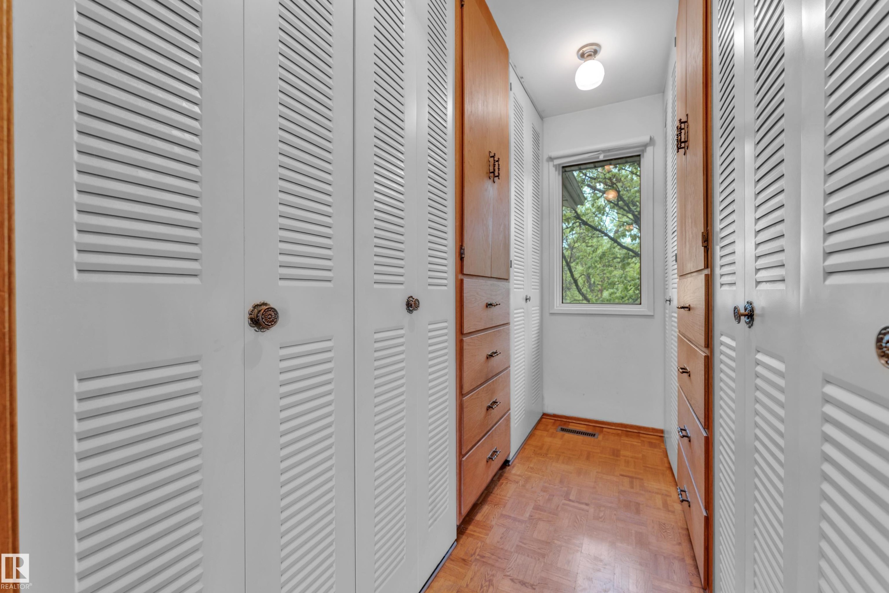 Hallway featuring louvered bi-fold closet doors, wood-finish flooring, and built-in wood cabinetry with drawers - 10819 54 Avenue, Edmonton, AB
