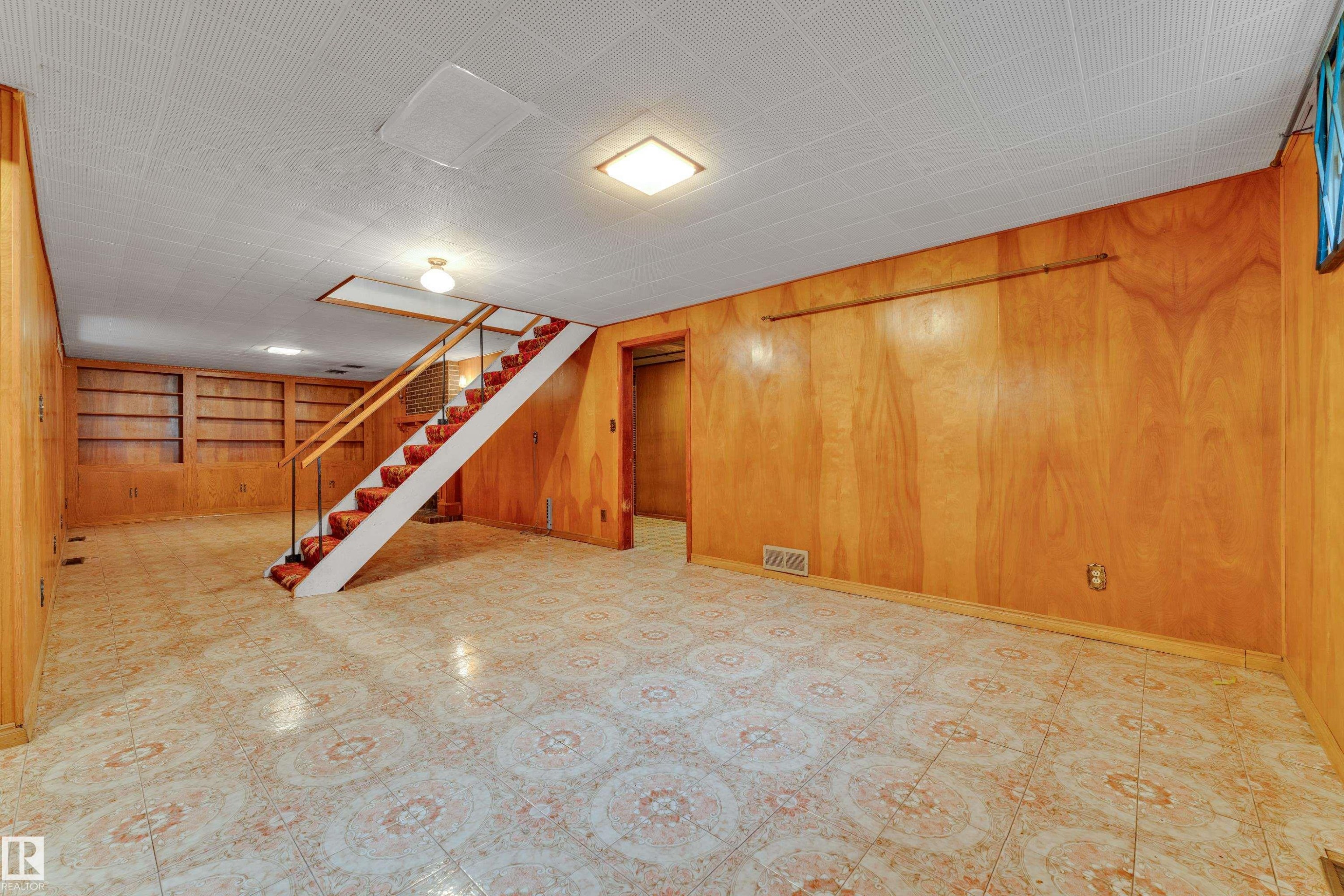 Spacious lower level featuring wood-finish wall paneling, patterned floor tiling, and a staircase with a wood handrail and metal balusters - 10819 54 Avenue, Edmonton, AB