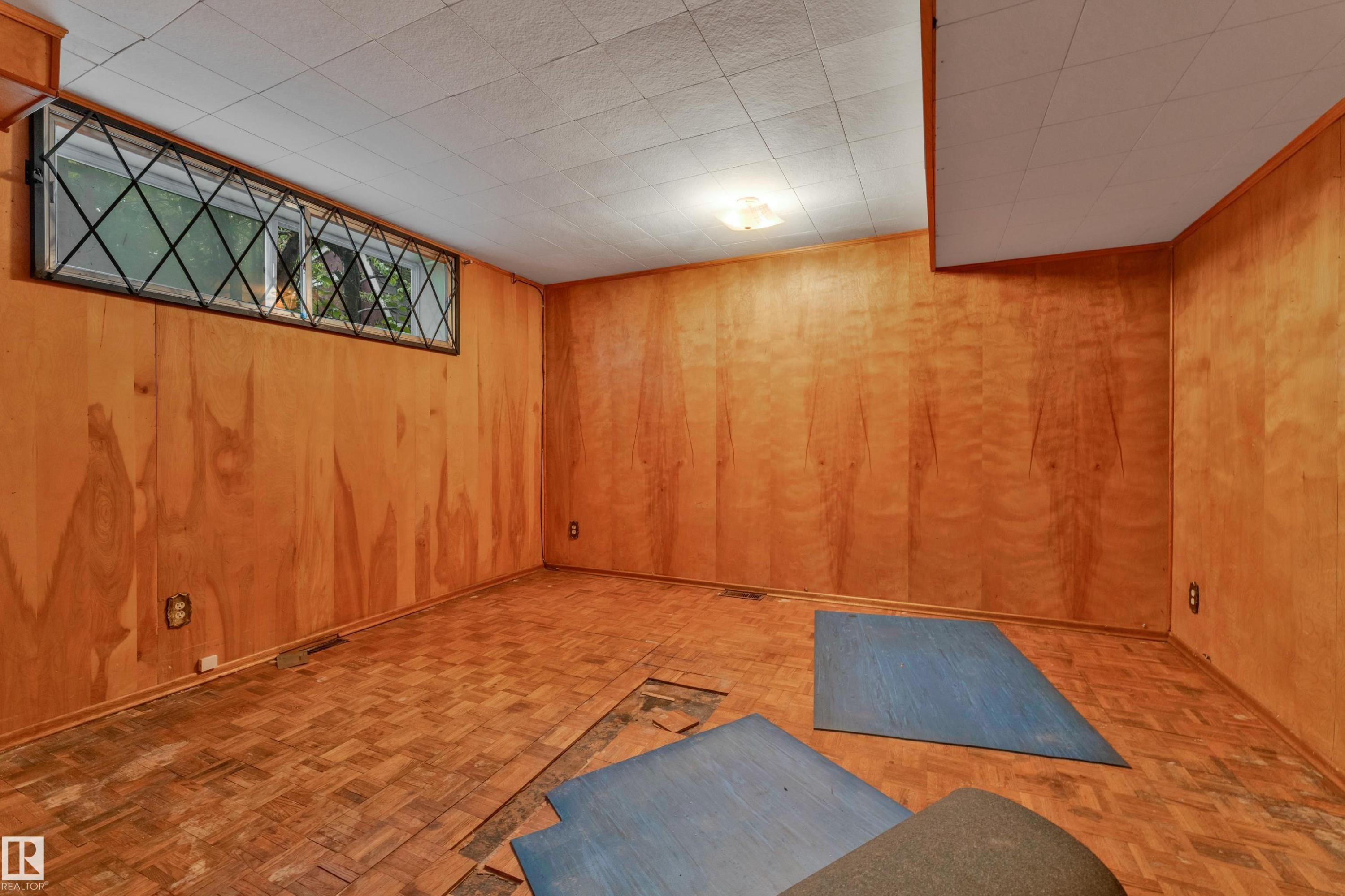 Room featuring wood-paneled walls, a drop ceiling, and parquet wood-finish flooring - 10819 54 Avenue, Edmonton, AB