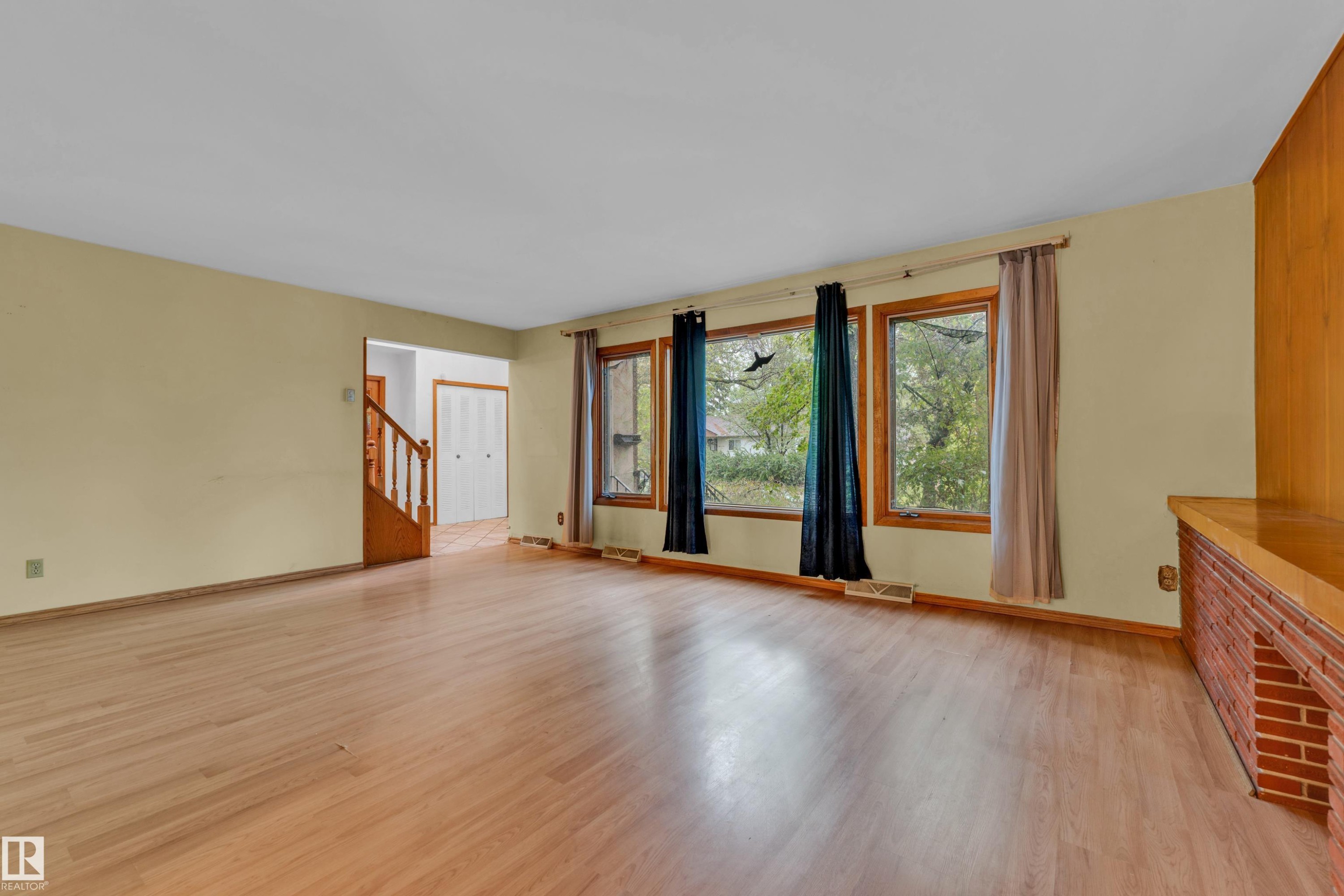 Spacious room featuring wood-finish flooring, a wall of three windows, and a built-in brick and wood-paneled structure - 10819 54 Avenue, Edmonton, AB