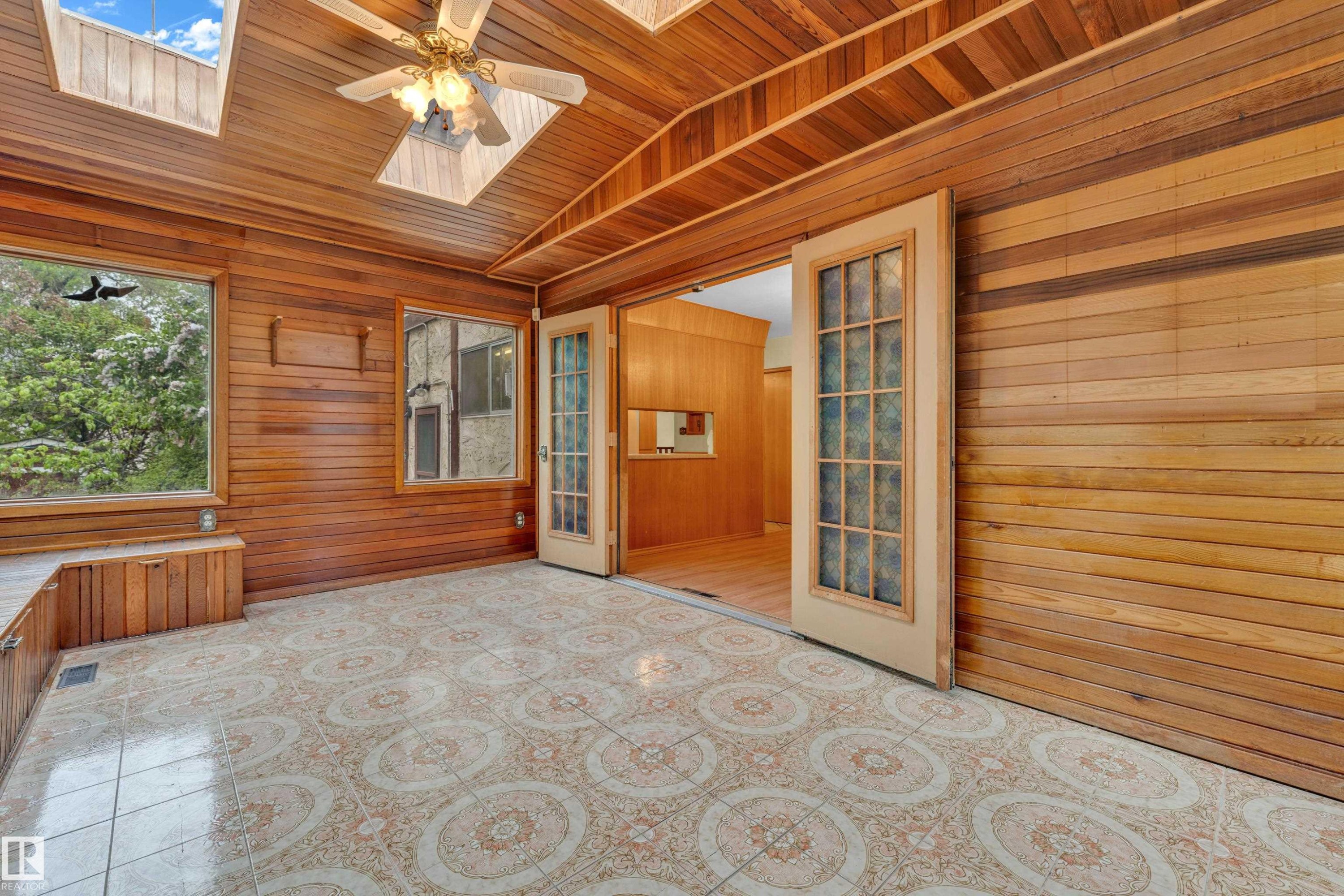 Sunroom featuring extensive natural wood paneling, patterned tile flooring, multiple windows, skylights, and a ceiling fan - 10819 54 Avenue, Edmonton, AB