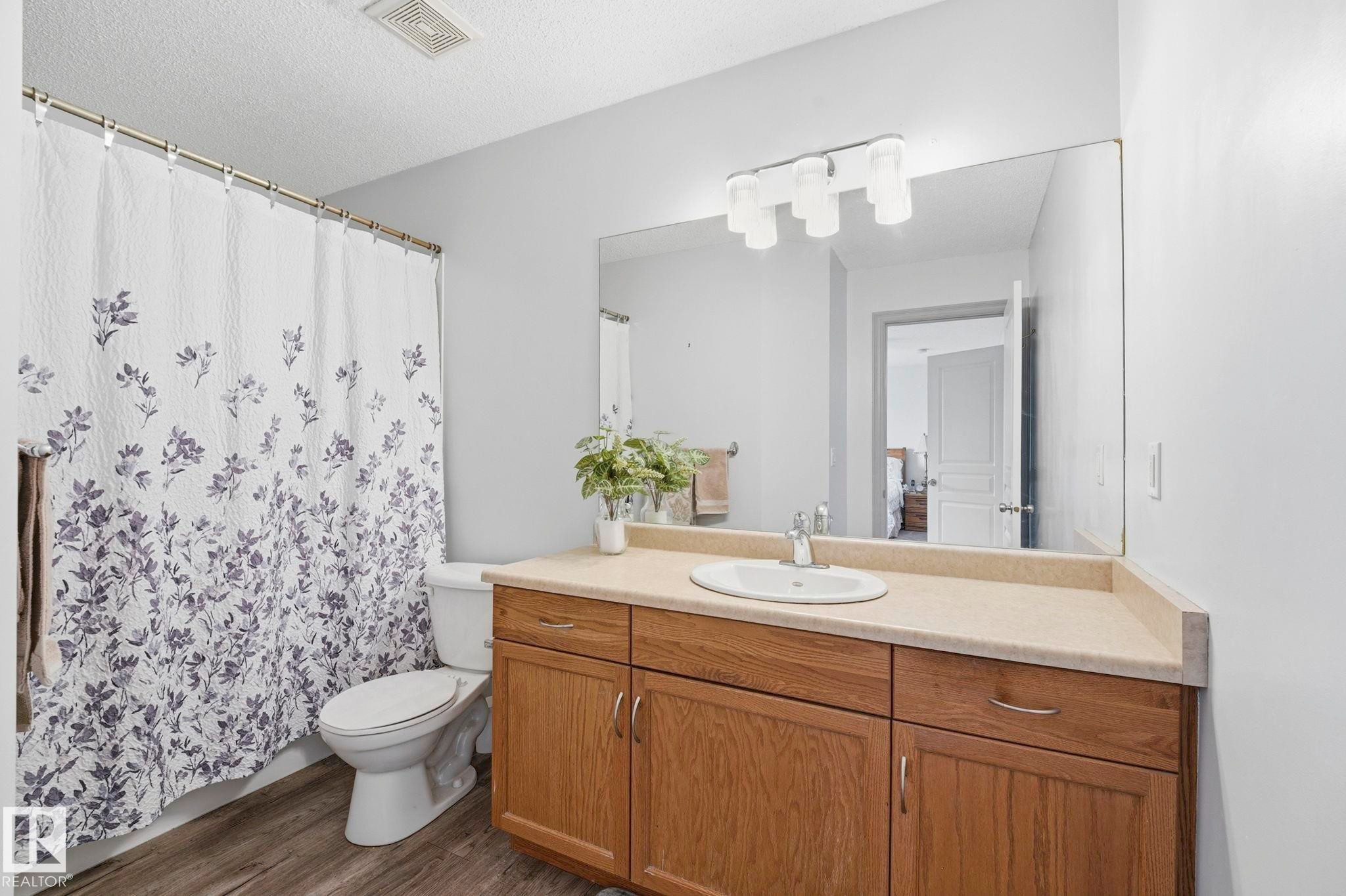 Bathroom featuring a wood-finish vanity with a light-toned countertop, an integrated sink with a chrome faucet, a large wall-mounted mirror, and overhead lighting - 3231 28A Avenue Nw, Edmonton, AB - Indoor Photo Showing Bathroom