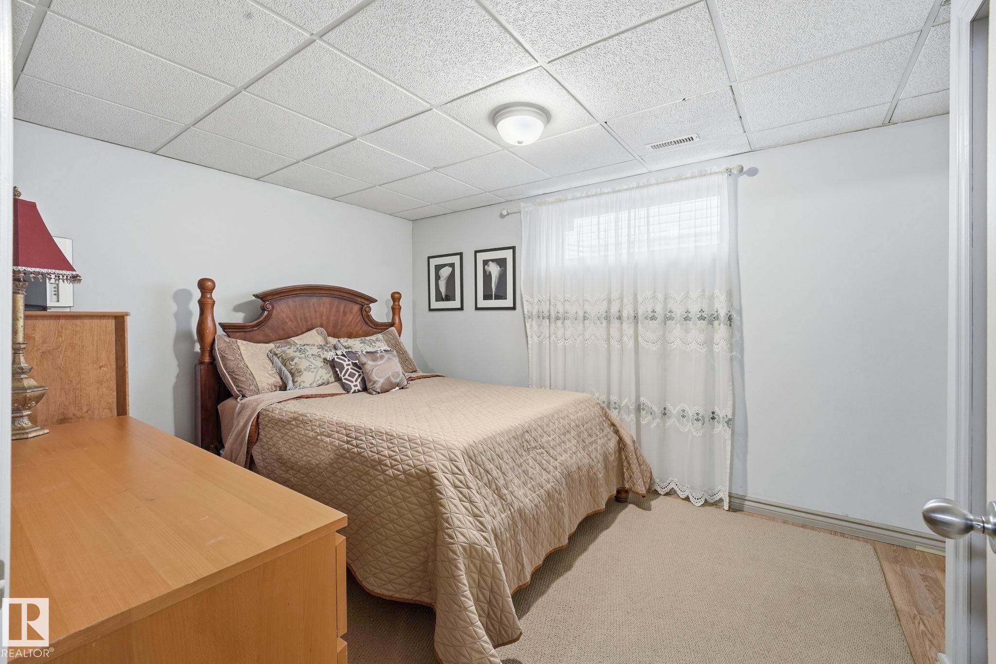 Bedroom featuring light gray walls, a textured drop ceiling, and a window with sheer curtains - 3231 28A Avenue Nw, Edmonton, AB - Indoor Photo Showing Bedroom