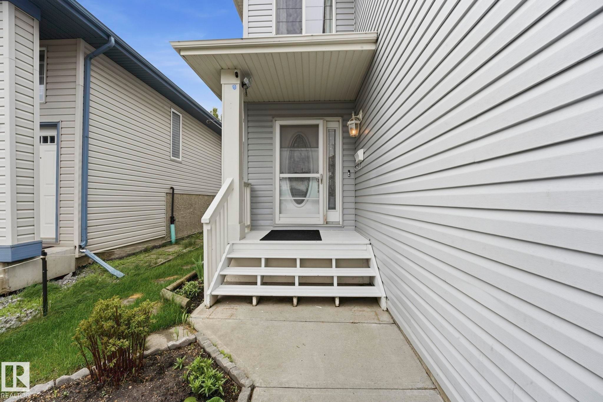 Front entrance with a covered porch, white railing, and exterior lighting fixture - 3231 28A Avenue Nw, Edmonton, AB - Outdoor
