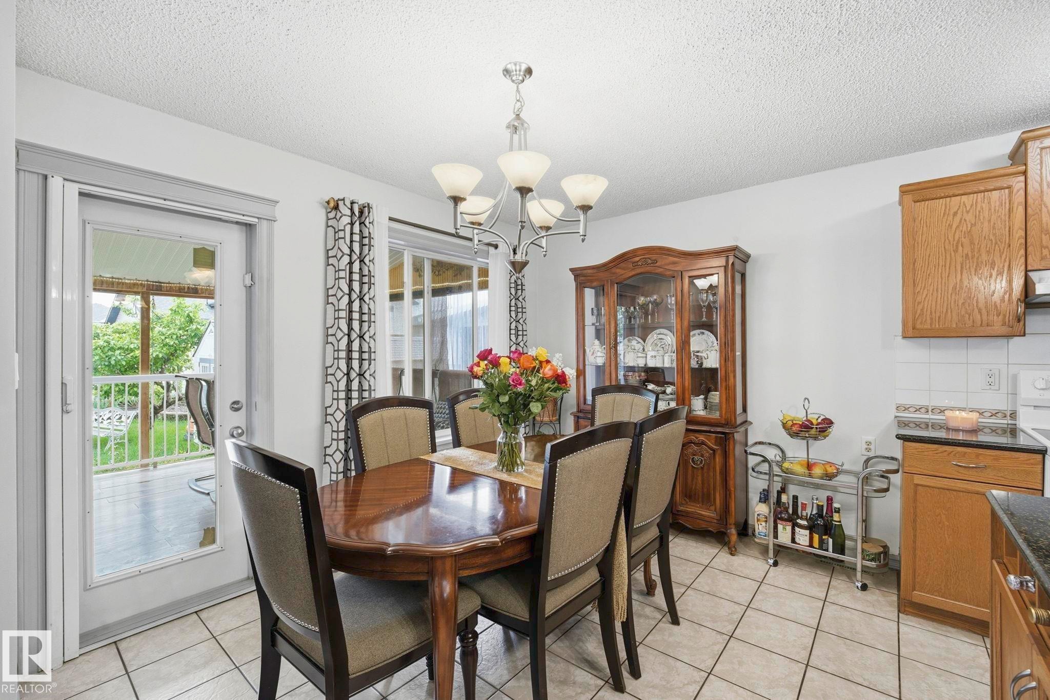 Dining area featuring neutral-toned tile flooring, a glass-paneled door leading to an exterior deck, and a multi-light chandelier - 3231 28A Avenue Nw, Edmonton, AB - Indoor Photo Showing Dining Room
