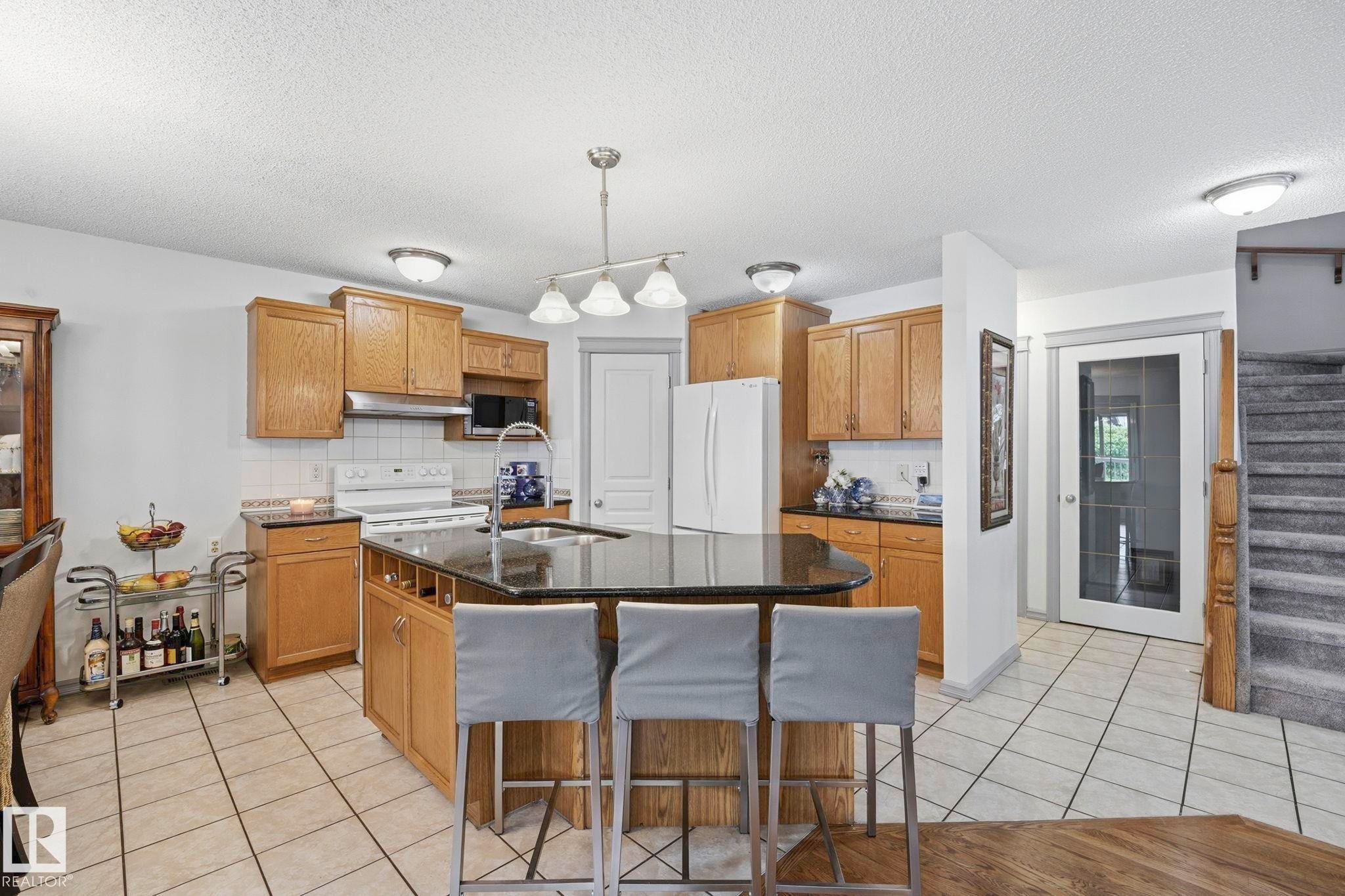 Kitchen featuring wood-finish cabinetry, black countertops, and a central island with integrated seating - 3231 28A Avenue Nw, Edmonton, AB - Indoor Photo Showing Kitchen