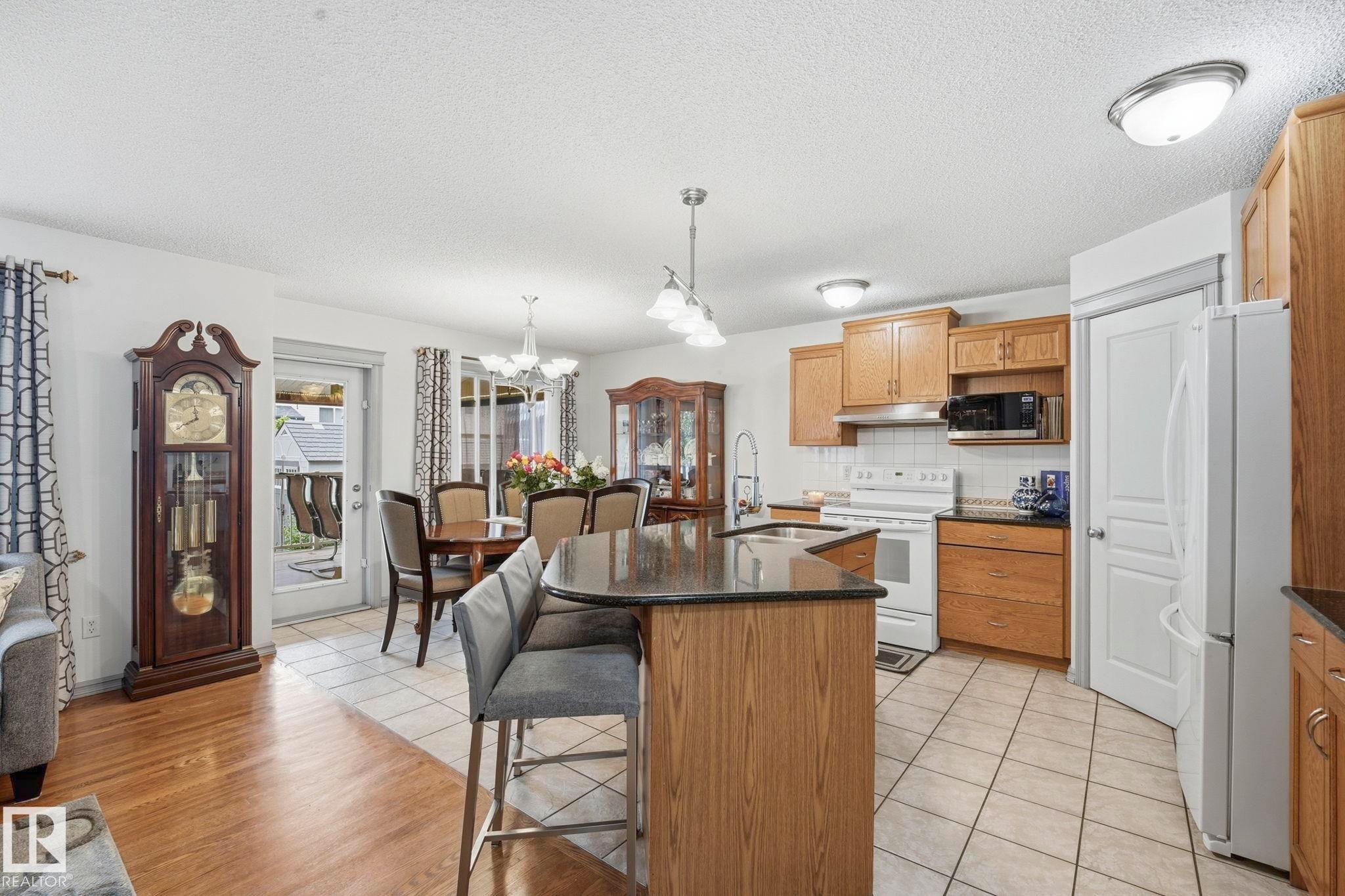 Open-concept kitchen and dining area featuring a breakfast bar with seating for two, wood cabinetry, stainless steel sink, and white appliances - 3231 28A Avenue Nw, Edmonton, AB - Indoor Photo Showing Kitchen With Double Sink
