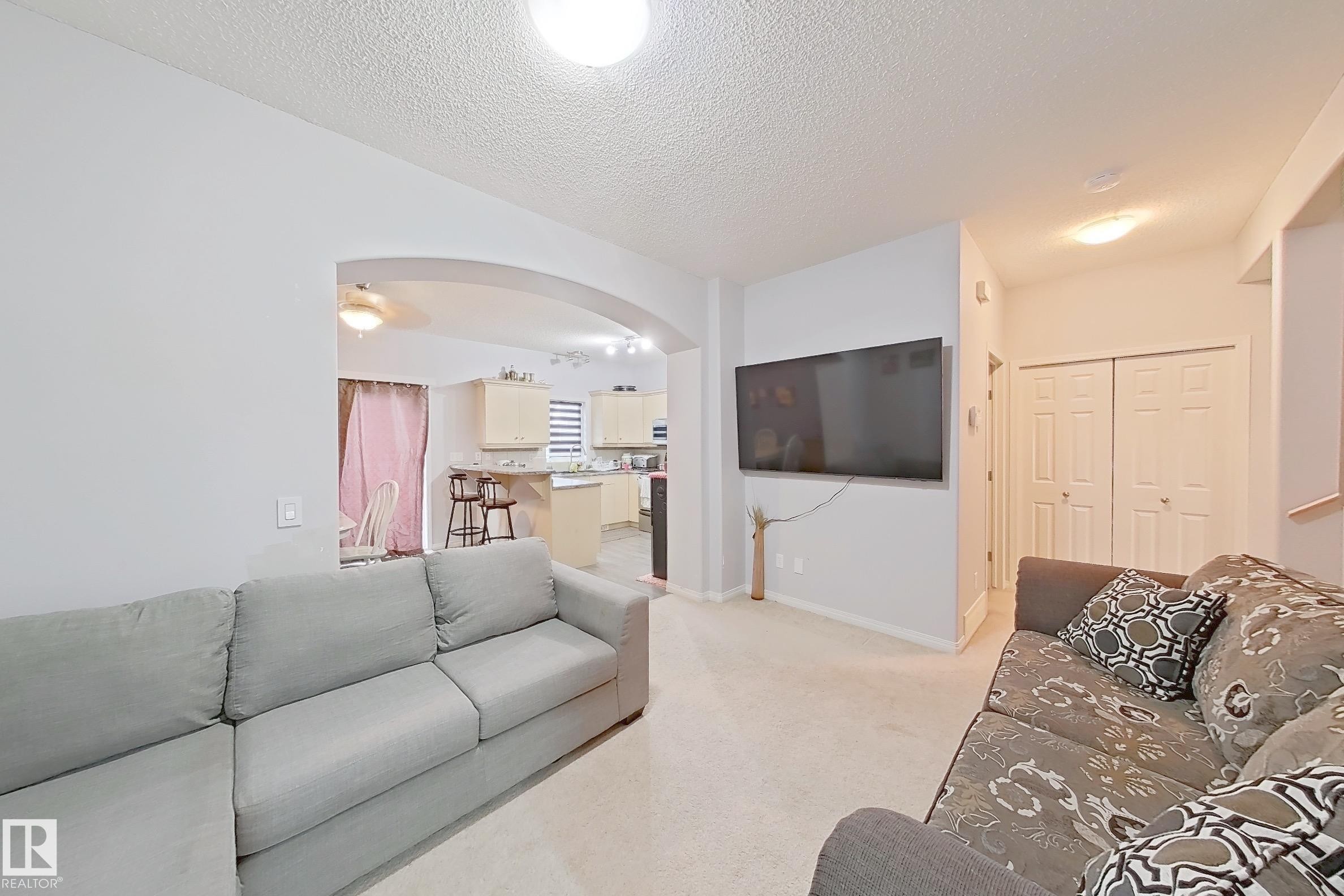 Open-concept living area with light-toned carpet flooring and neutral wall finishes - 41 5102 30 Avenue, Beaumont, AB