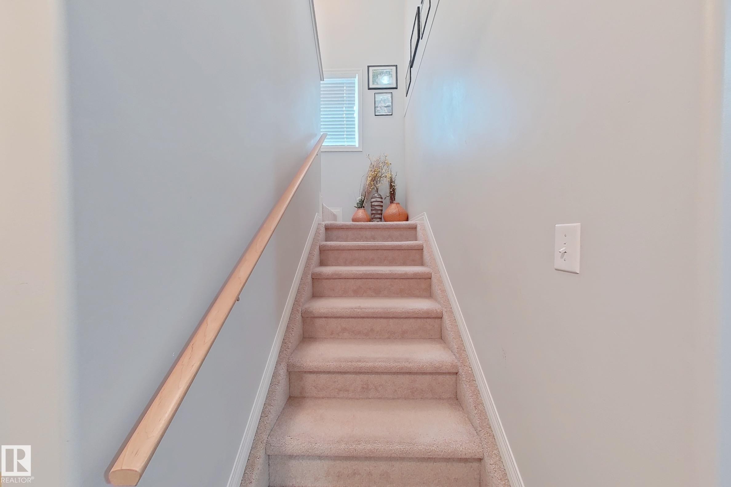 Carpeted staircase featuring a light wood handrail and a window with horizontal blinds - 41 5102 30 Avenue, Beaumont, AB