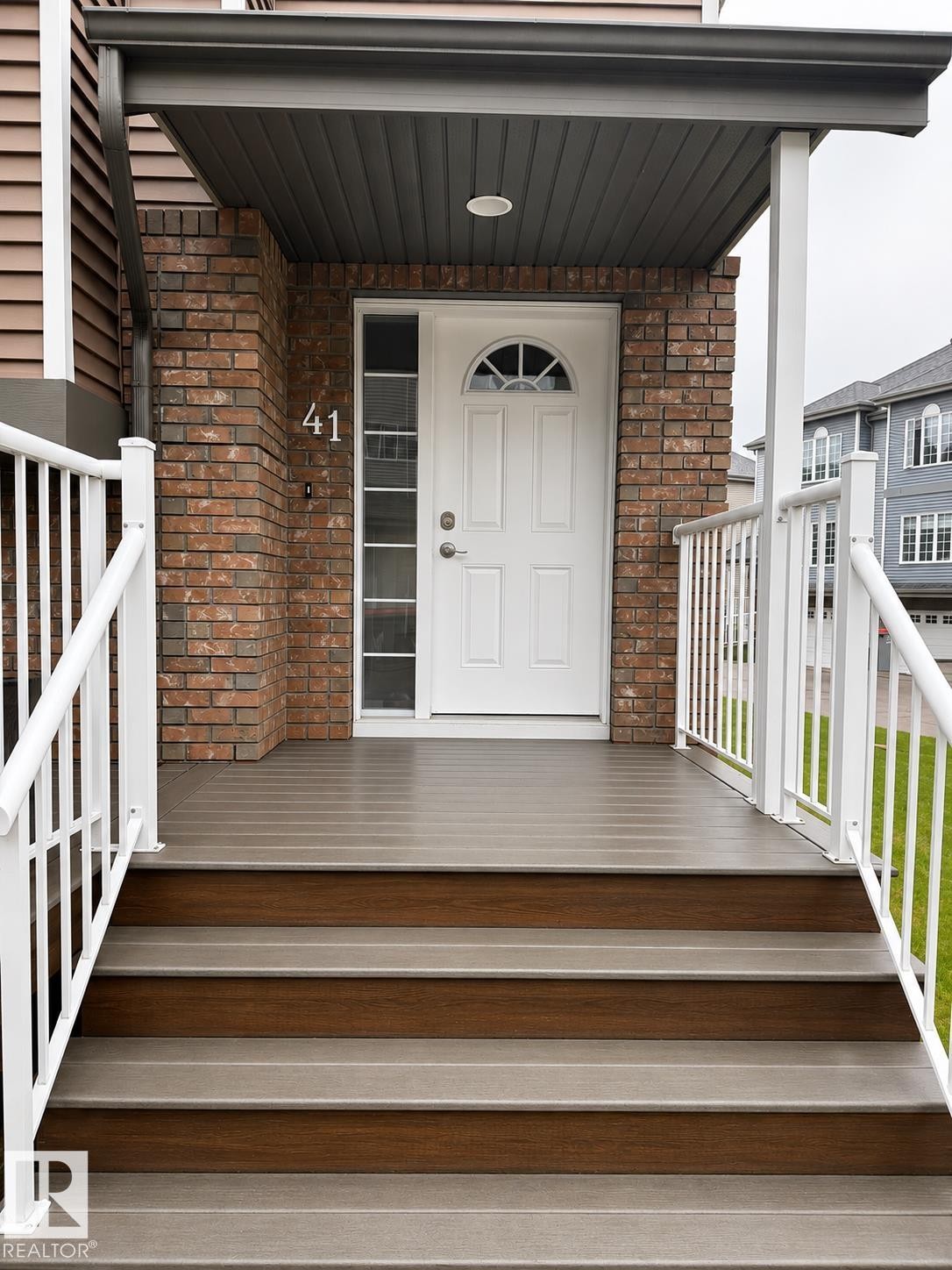 Front entrance featuring a white panel door with an arched window, brick facade, composite decking, white railings, and a recessed overhead light - 41 5102 30 Avenue, Beaumont, AB
