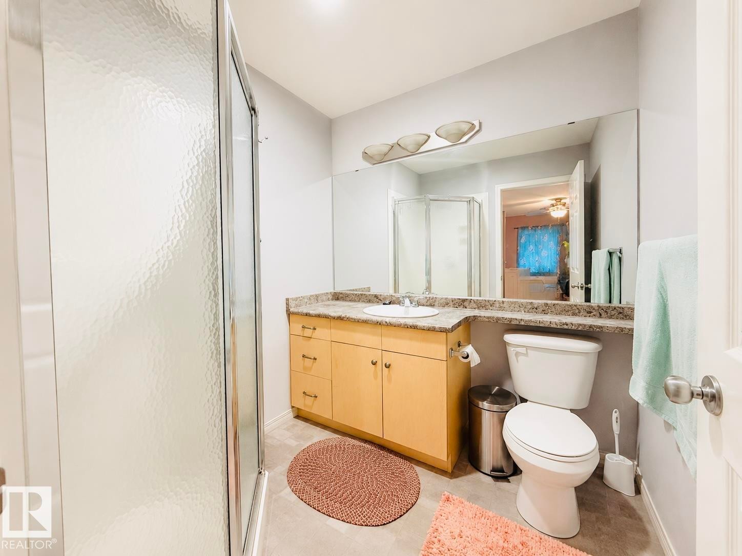 Bathroom featuring a glass-enclosed shower, light wood-finish vanity with a single basin sink, speckled countertop, and a large wall-mounted mirror - 41 5102 30 Avenue, Beaumont, AB