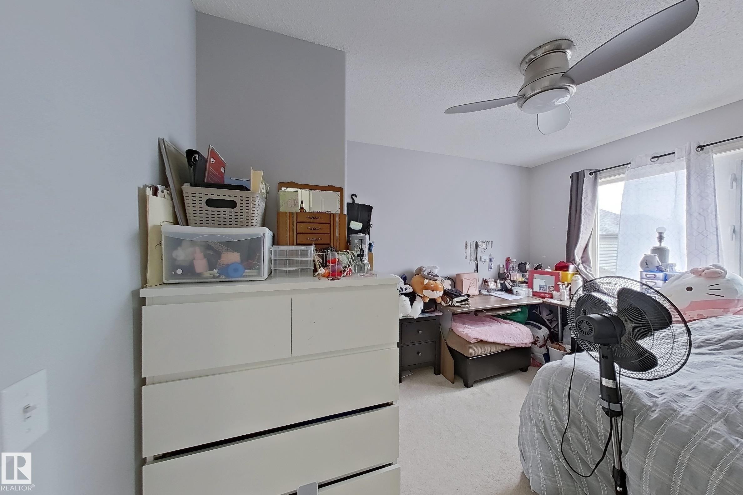 Carpeted room with a ceiling fan featuring integrated lighting, light-toned walls, and a window with a dark curtain rod - 41 5102 30 Avenue, Beaumont, AB