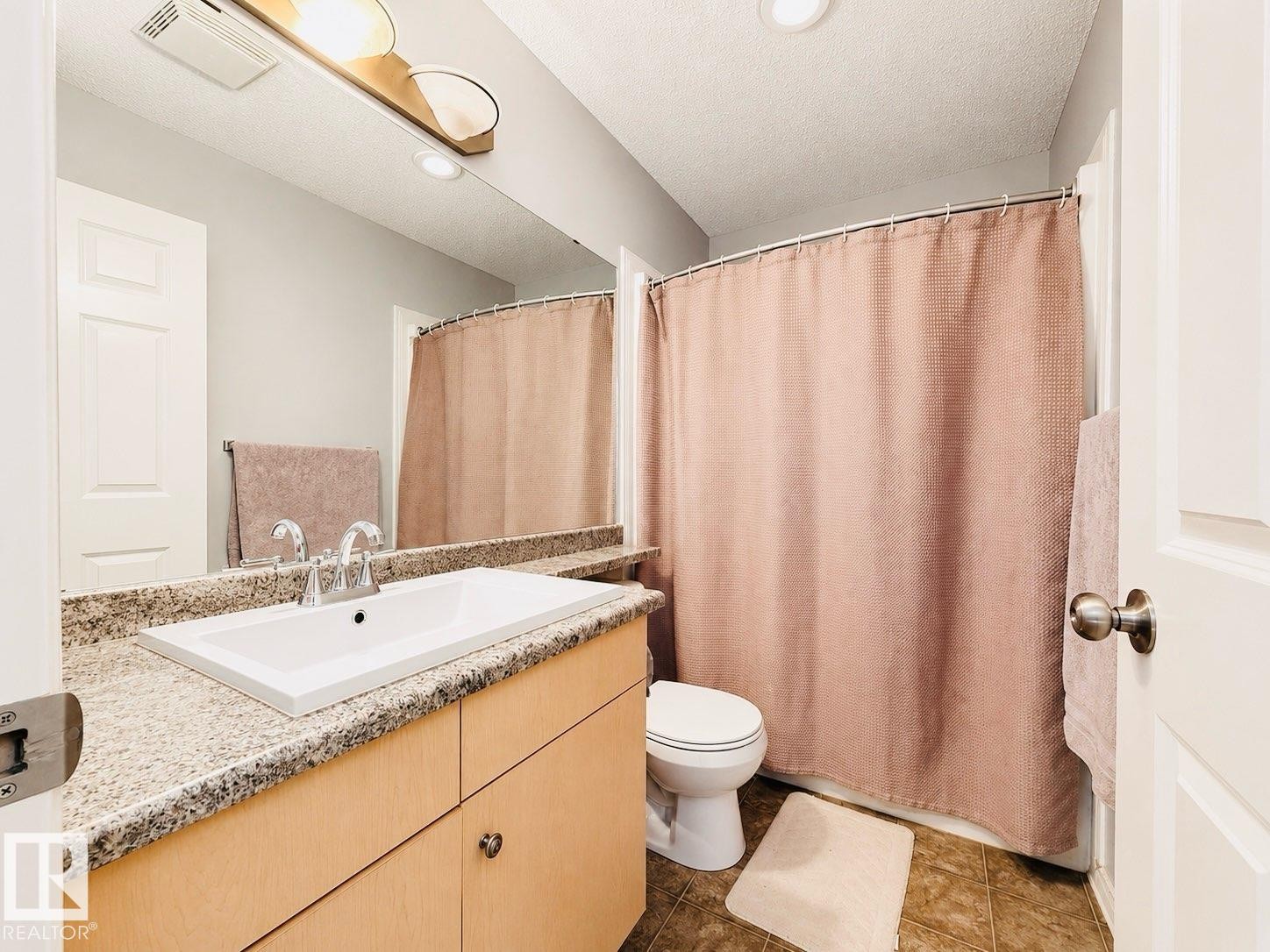 Bathroom featuring a wood-finish vanity with a granite-style countertop, an integrated rectangular sink, and a chrome faucet - 41 5102 30 Avenue, Beaumont, AB