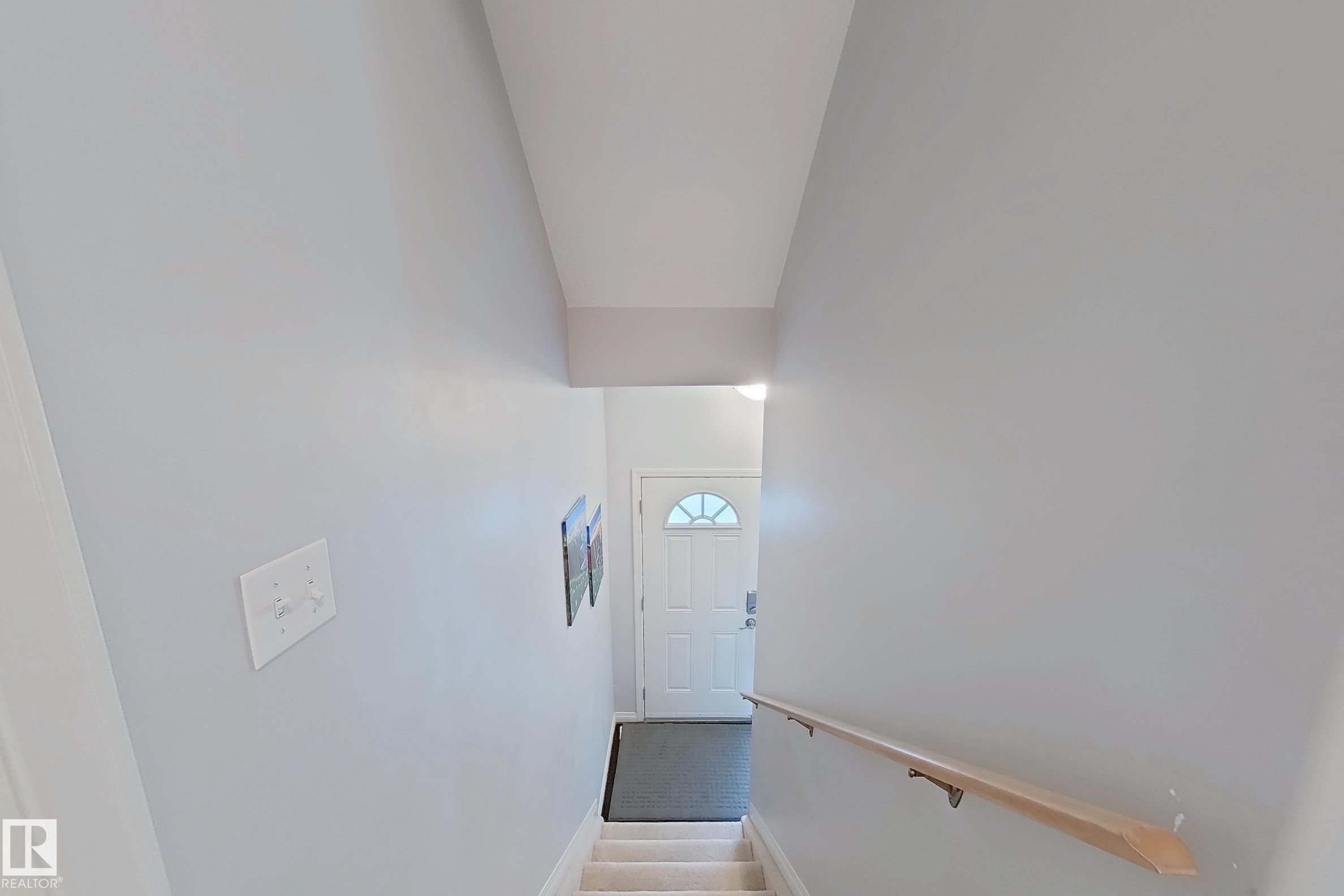 Carpeted staircase descending towards a front entry door with a decorative half-moon window - 41 5102 30 Avenue, Beaumont, AB