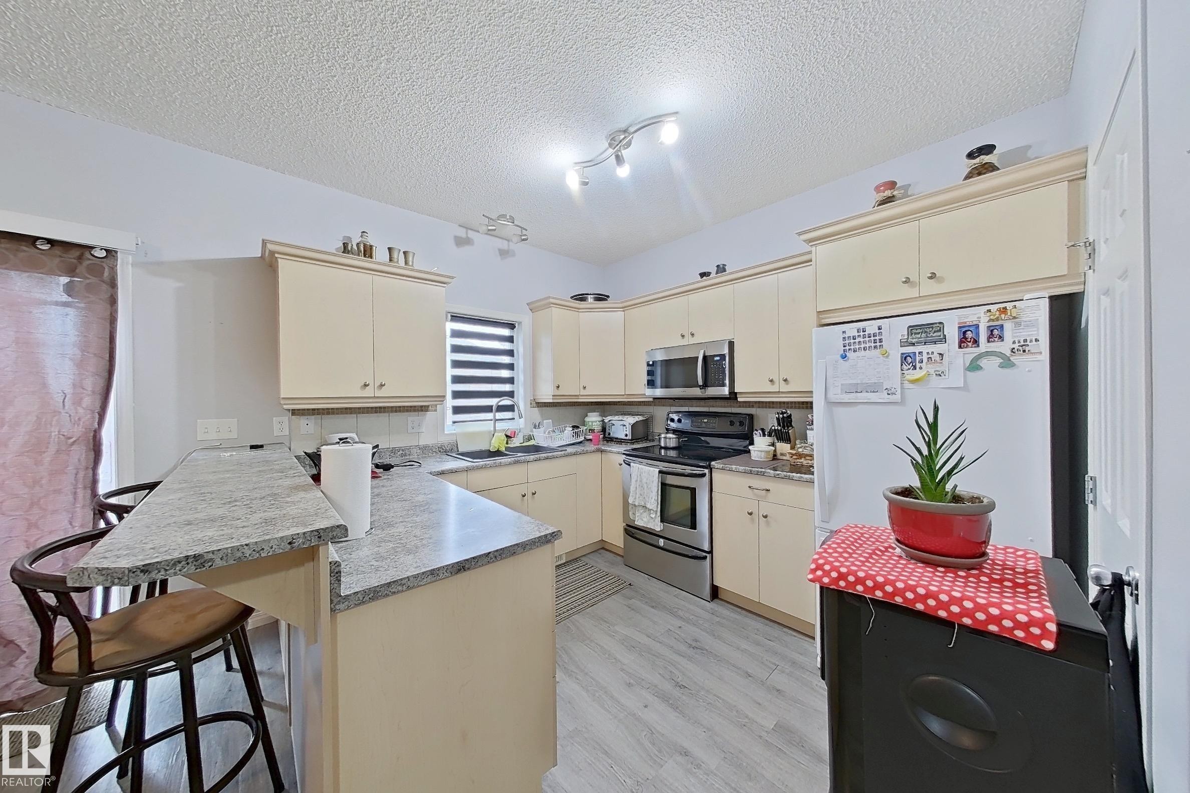 Kitchen featuring light-toned cabinetry, light-colored countertops, stainless steel appliances, and wood-finish flooring - 41 5102 30 Avenue, Beaumont, AB