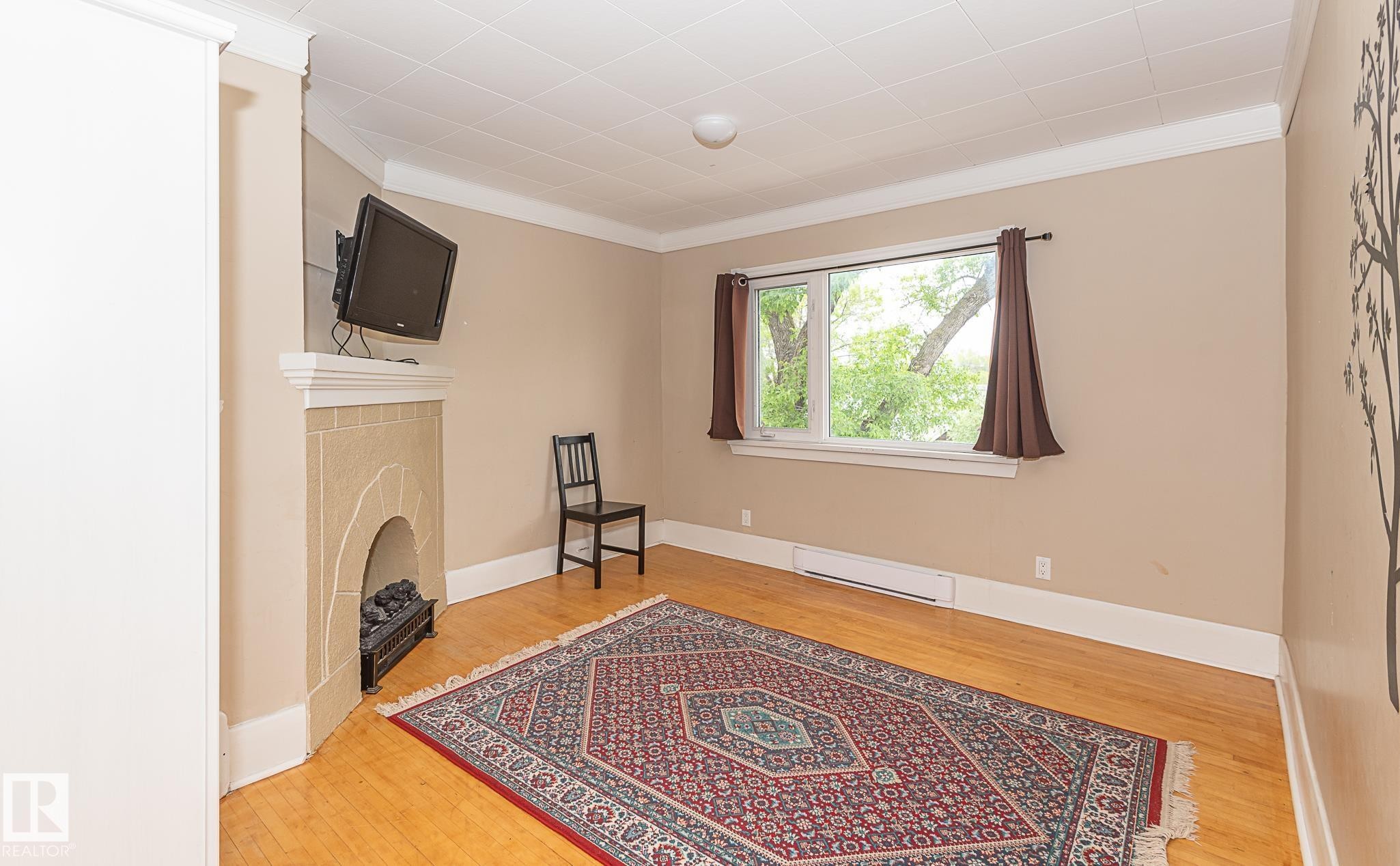 Room featuring wood-finish flooring, a decorative fireplace, and a large window providing ample natural light - 9623 110A Avenue, Edmonton, AB