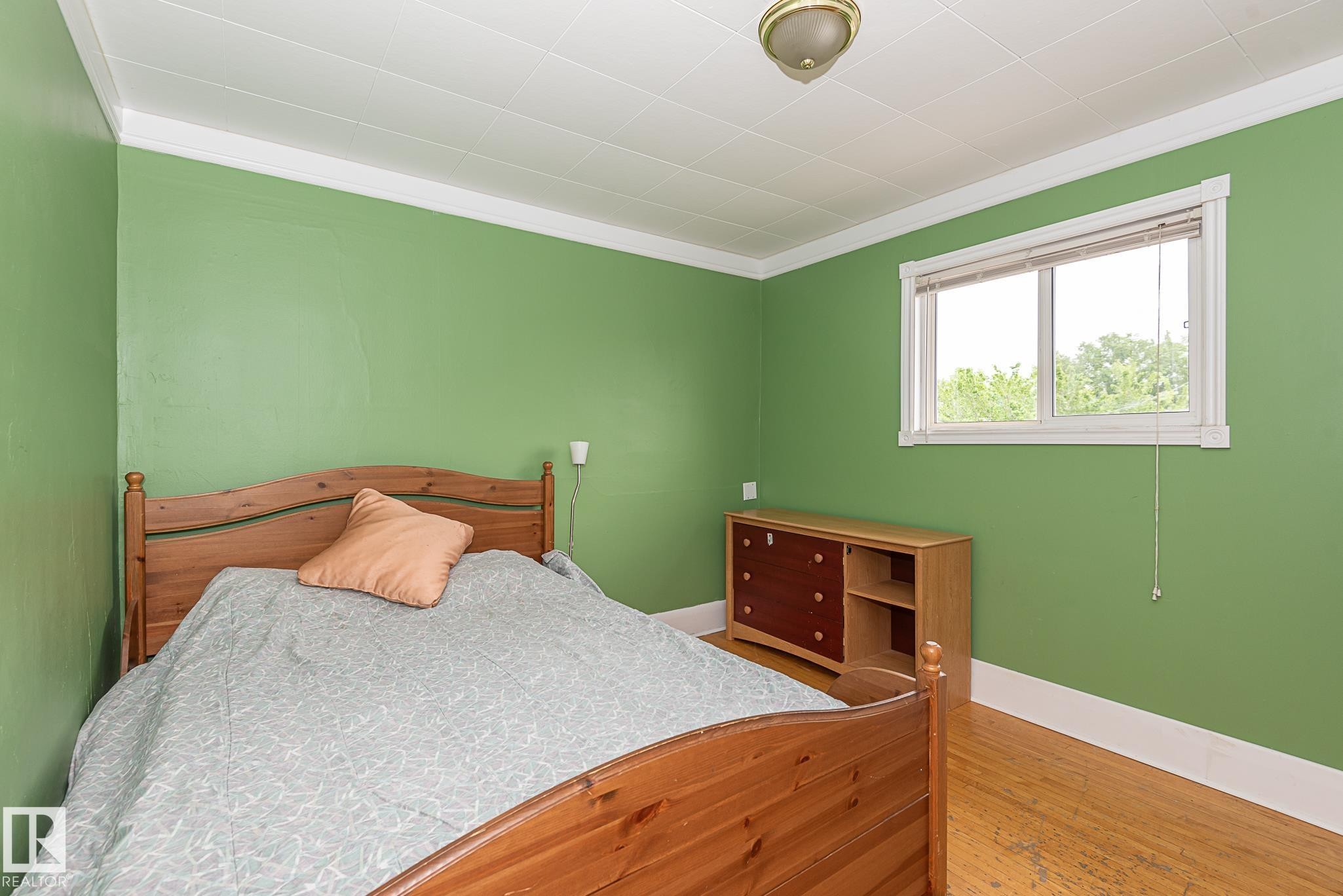 Room featuring wood-finish flooring, a window with exterior tree scenery, a built-in light fixture, and white baseboards and crown molding - 9623 110A Avenue, Edmonton, AB