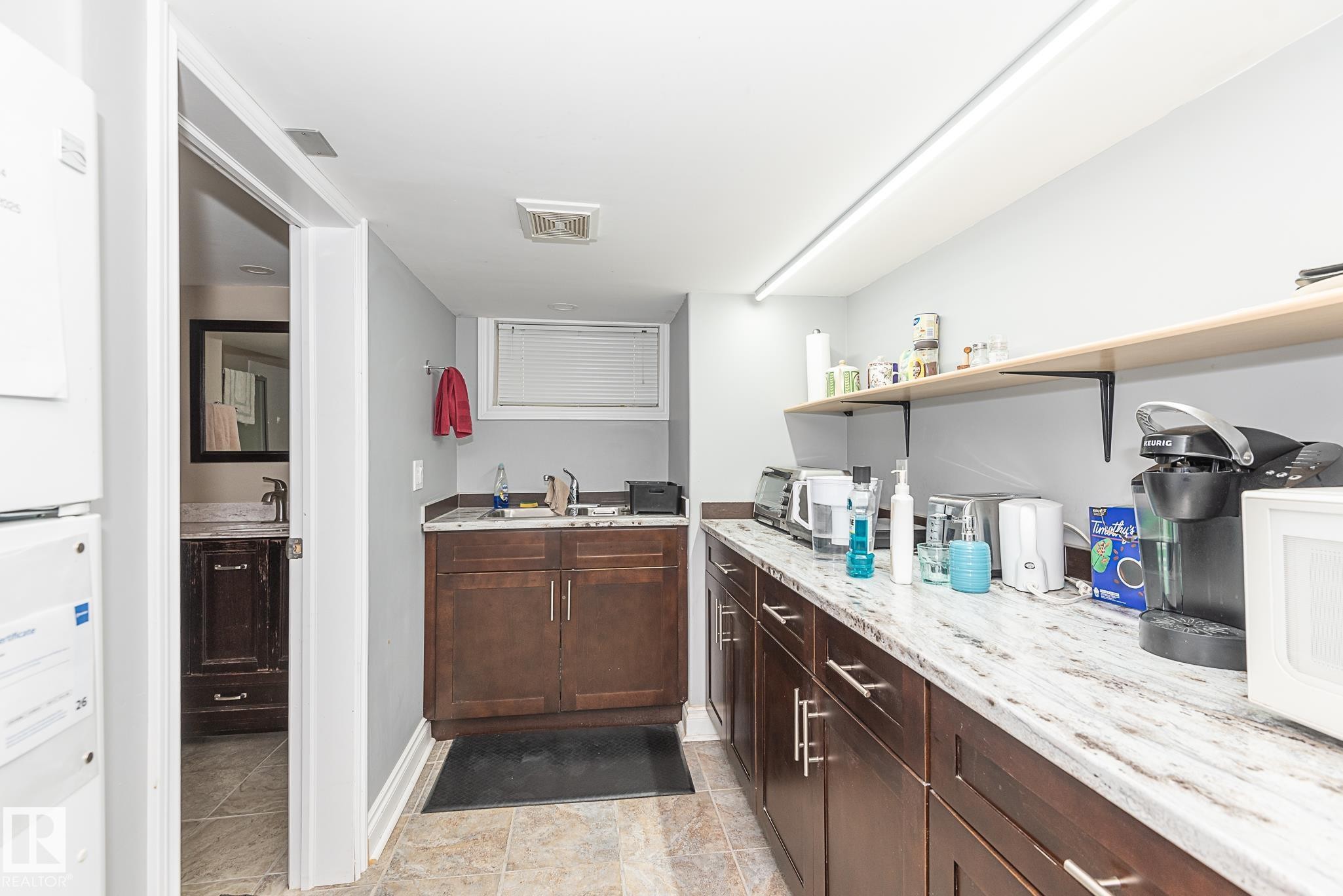 Functional kitchen area featuring extensive counter space with a light-toned, patterned surface, rich wood-finish base cabinetry, a built-in sink, and open shelving - 9623 110A Avenue, Edmonton, AB