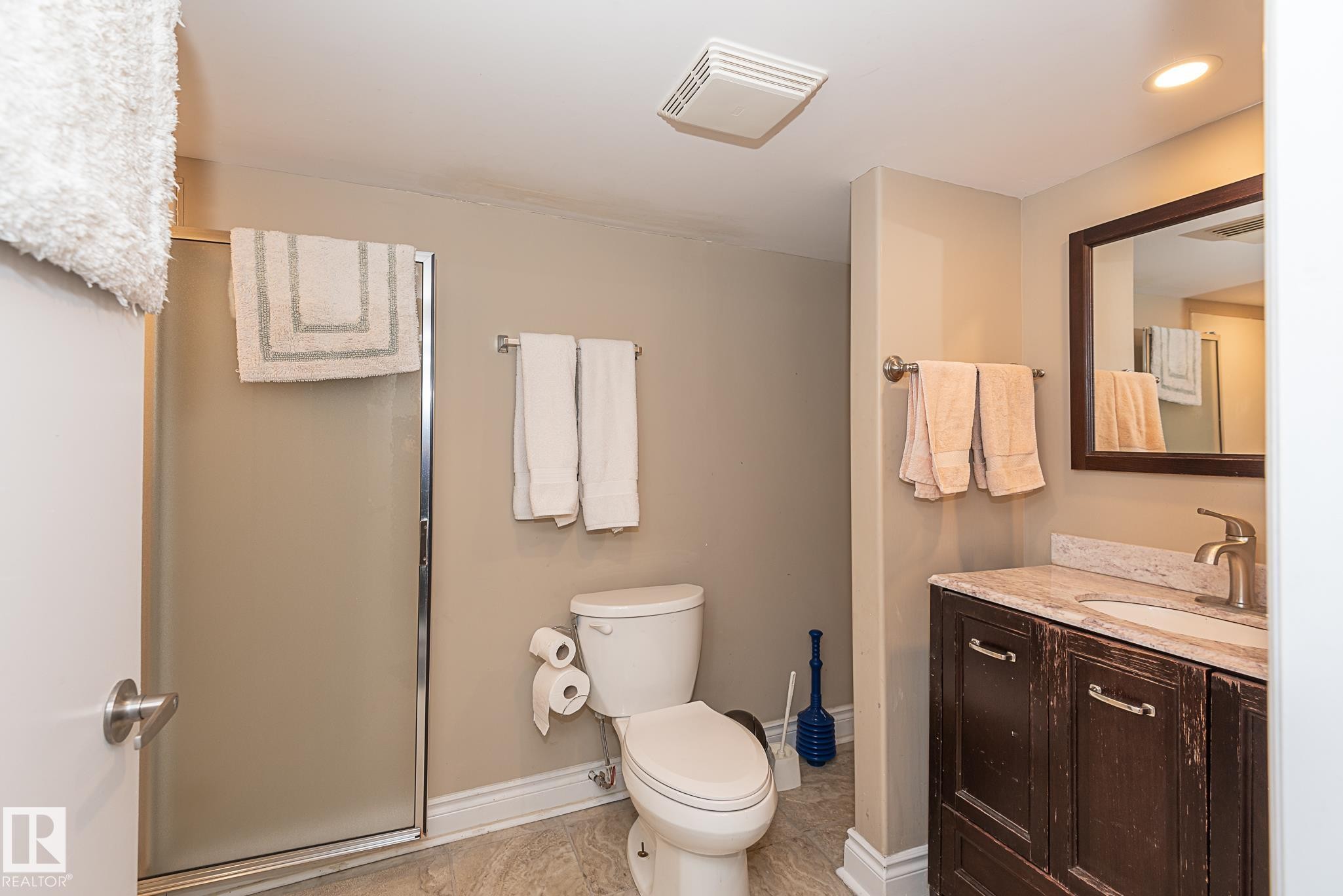 Full bathroom featuring a shower with a frosted glass enclosure, a white toilet, and a vanity with a light-colored countertop and a dark wood-finish cabinet - 9623 110A Avenue, Edmonton, AB